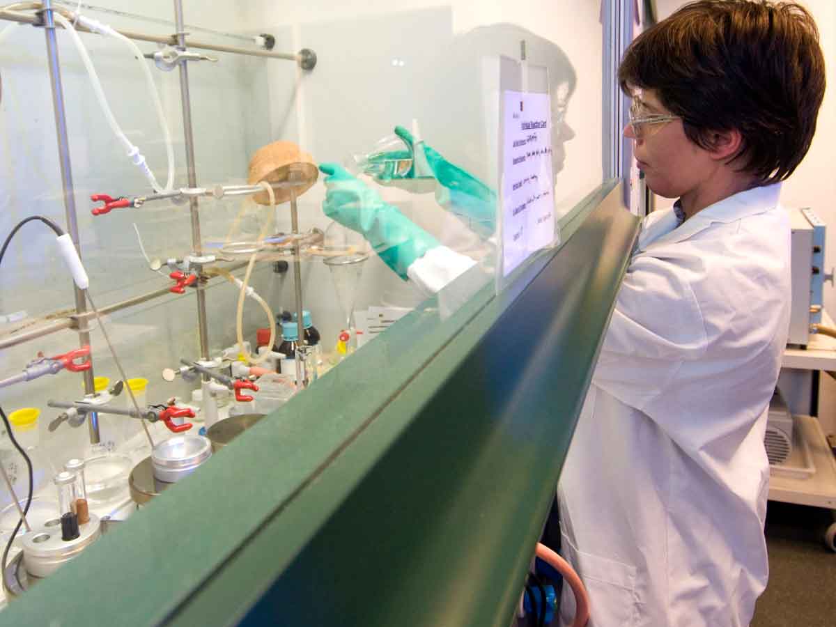 Scientist in protective gear working with glassware inside Mural Oncology’s laboratory fume hood during cancer-drug research