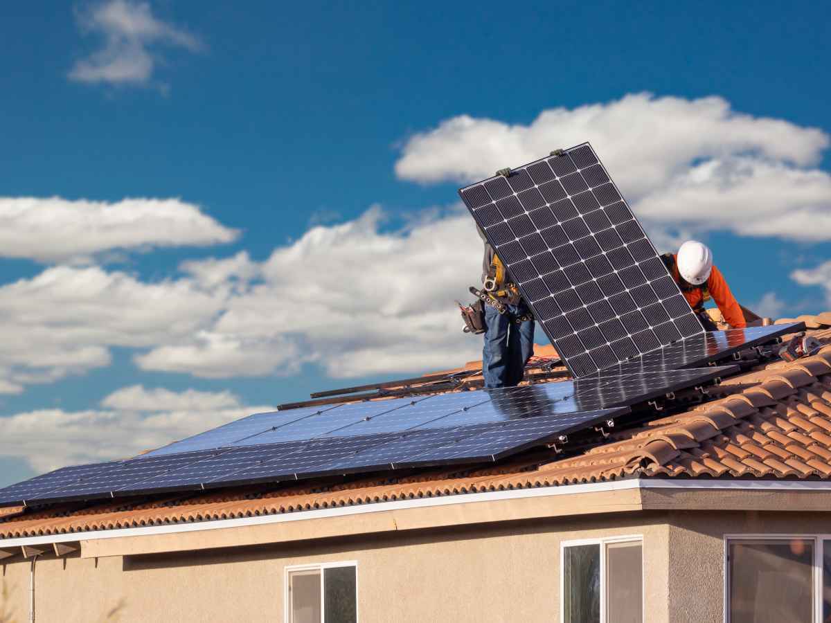 Workers installing solar panels on a residential rooftop under a blue sky with scattered clouds