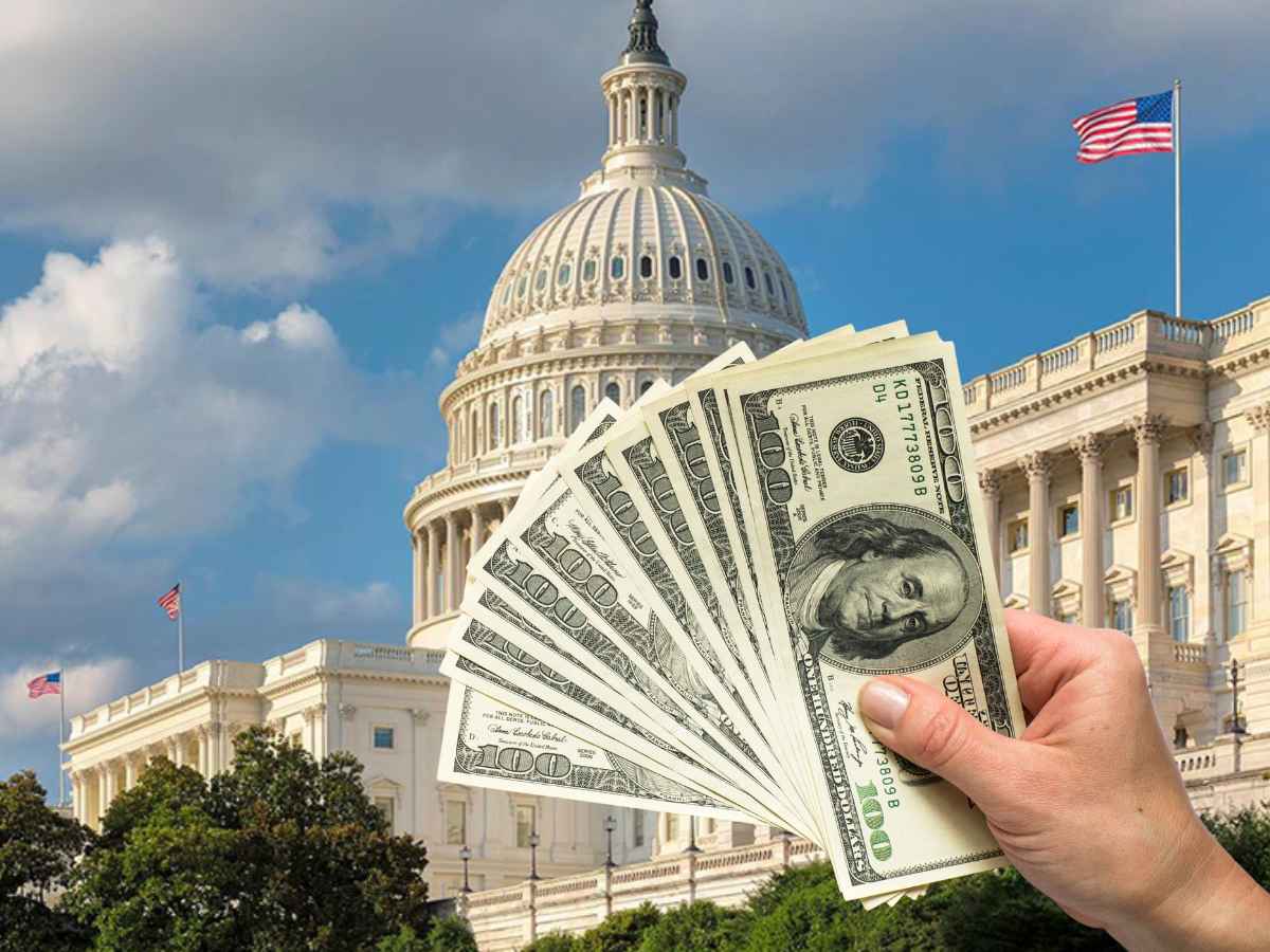 Hand holding US dollar bills in front of the Capitol building, representing federal financial aid and government benefits in the United States