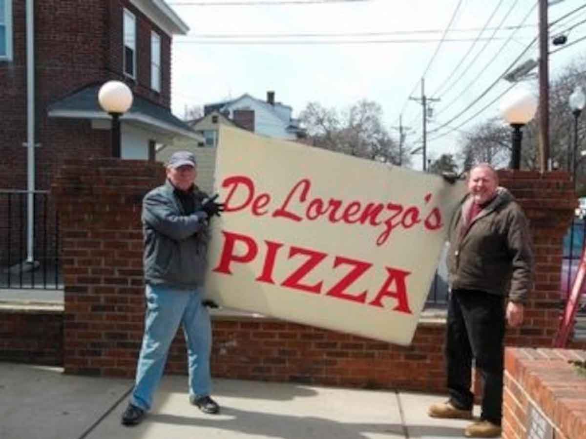 Two men hold the DeLorenzo’s Pizza sign outside the historic Hamilton, NJ restaurant after its reopening following a state tax shutdown