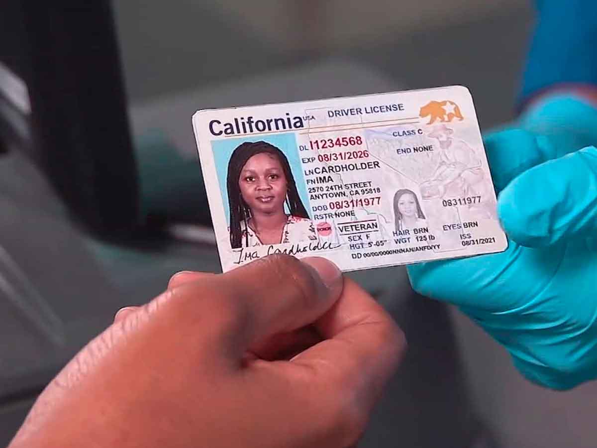 California DMV worker hands a Real ID–compliant driver’s license to an applicant during the in-person application process