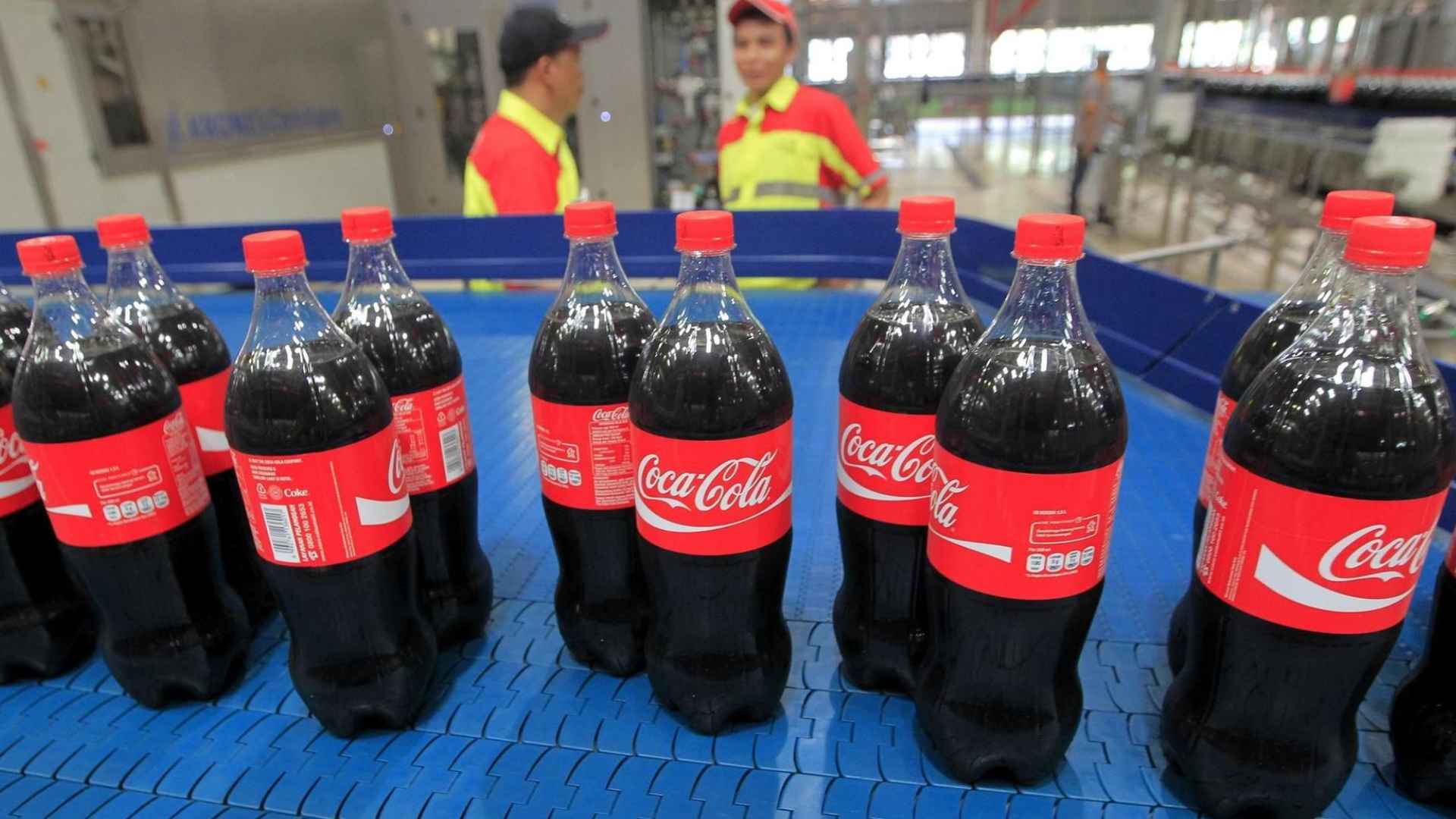 Coca-Cola PET bottles on a conveyor belt in an Indian bottling plant, illustrating the new 30 % recycled-plastic mandate.