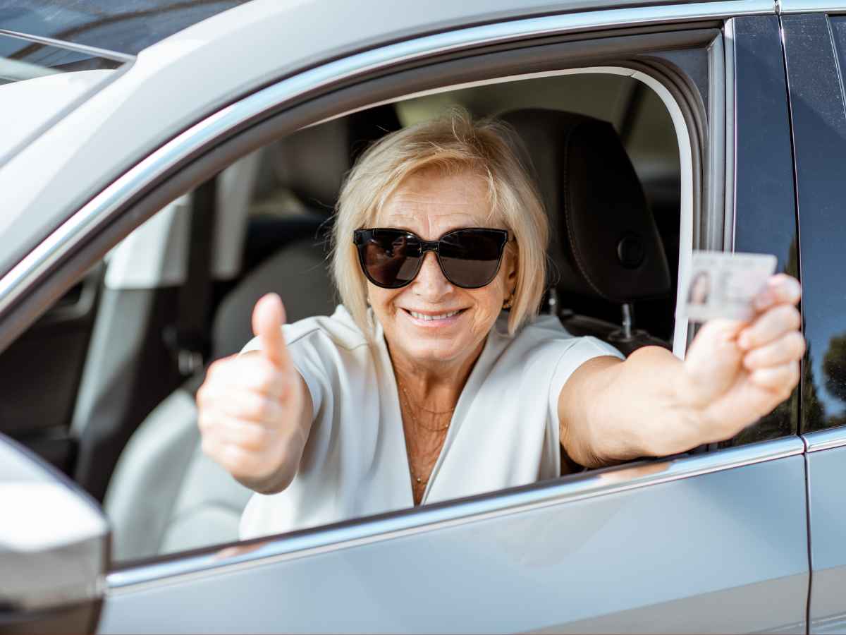 Senior woman smiling in car showing driver’s license and giving thumbs up, representing DMV law change in North Carolina