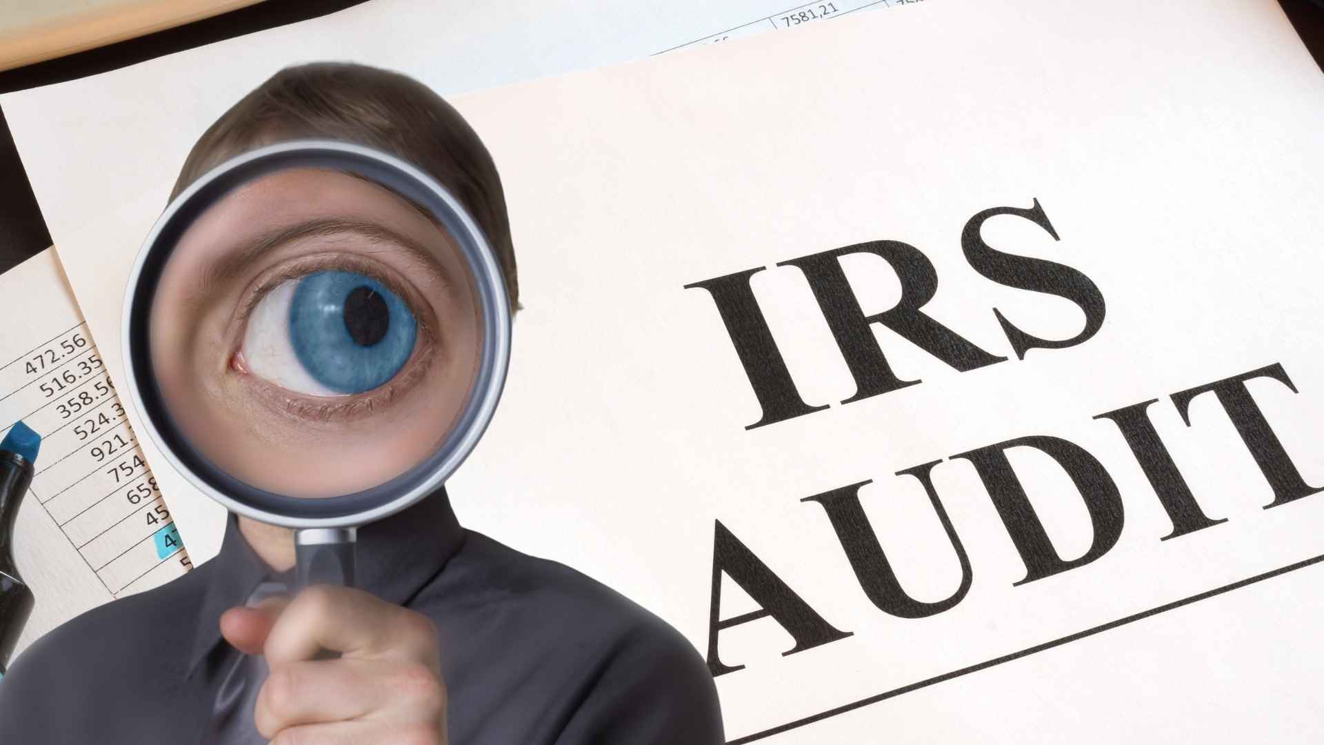 Magnifying glass enlarges a taxpayer’s eye beside an “IRS audit” document, symbolizing stricter scrutiny of false expenses