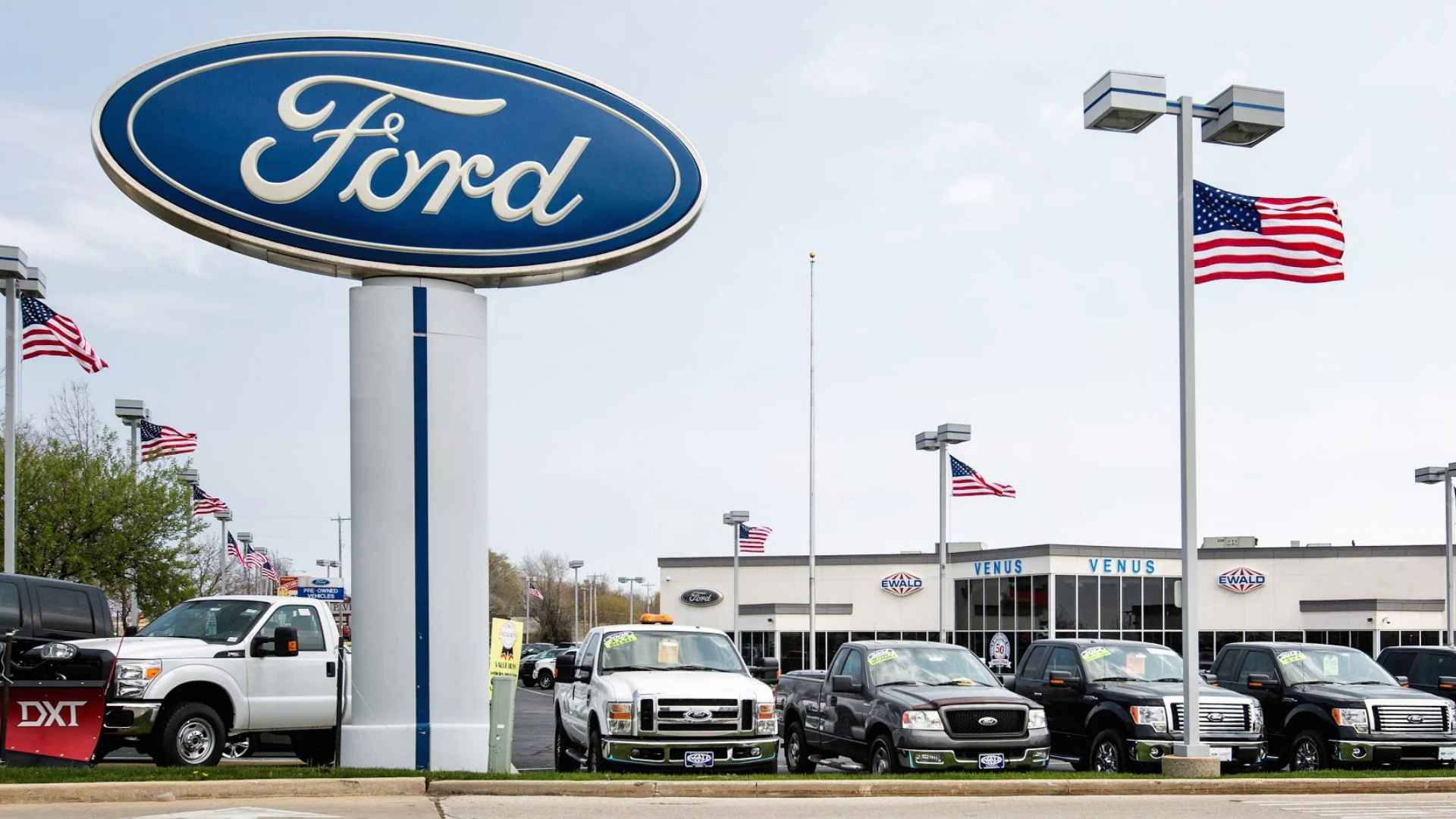 ford dealership lot with Ford logo sign, Super Duty trucks and SUVs parked under American flags