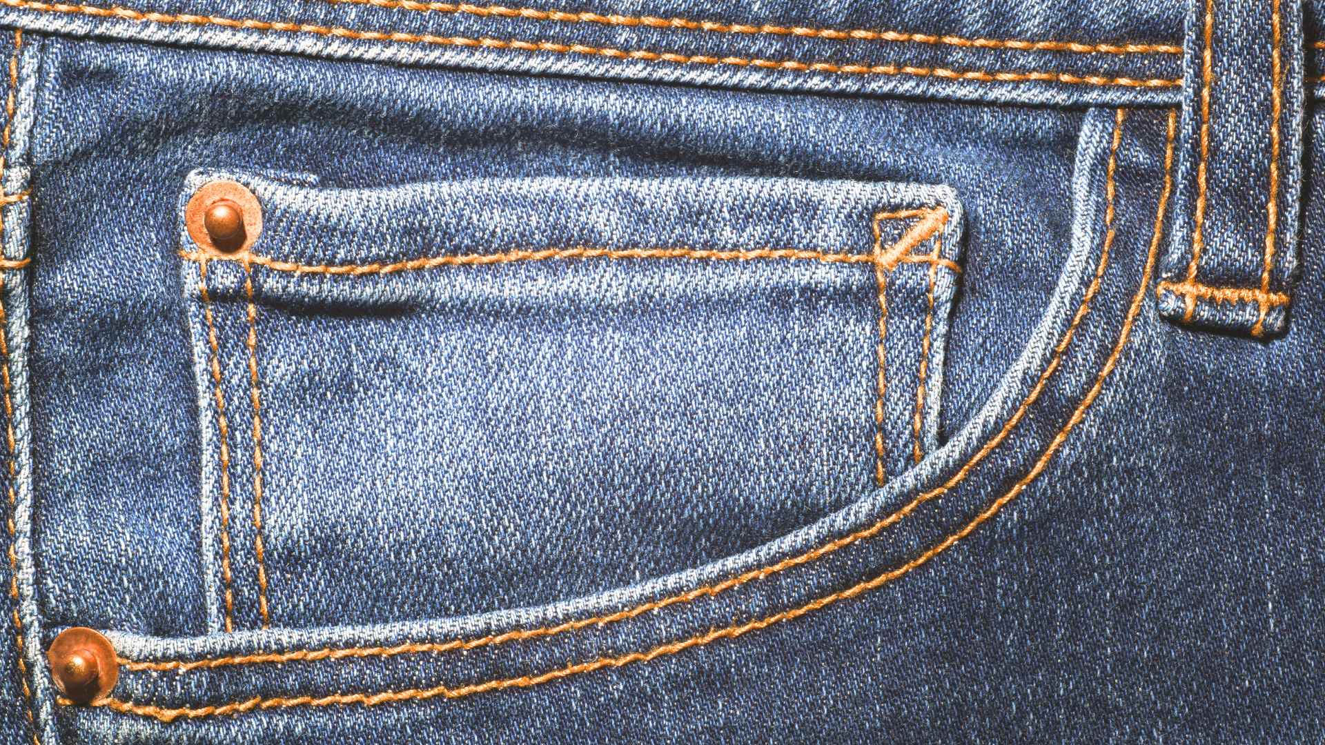 Close-up of blue denim pocket with copper metal rivets reinforcing the corners for added strength and durability