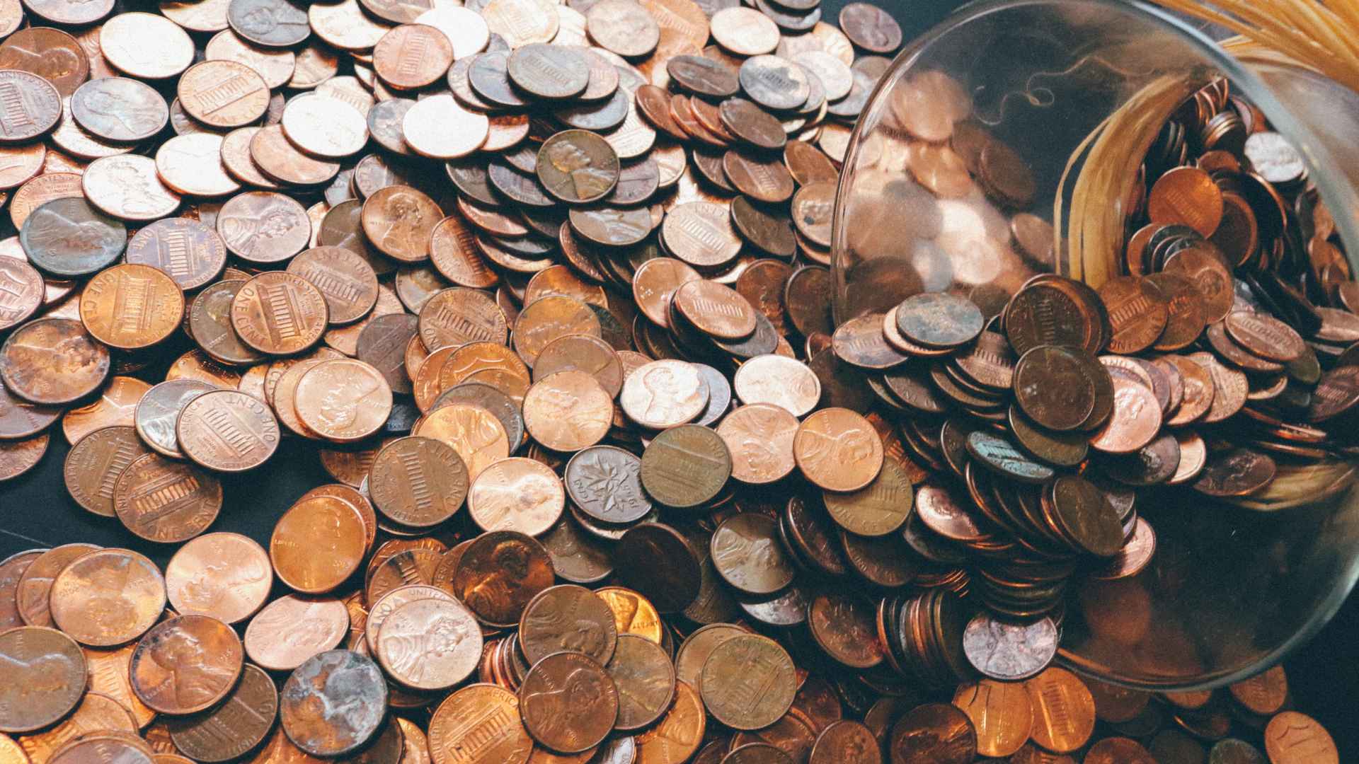 Glass jar spilling U.S. pennies, illustrating British government’s plan to retire the one-cent coin and save costs.