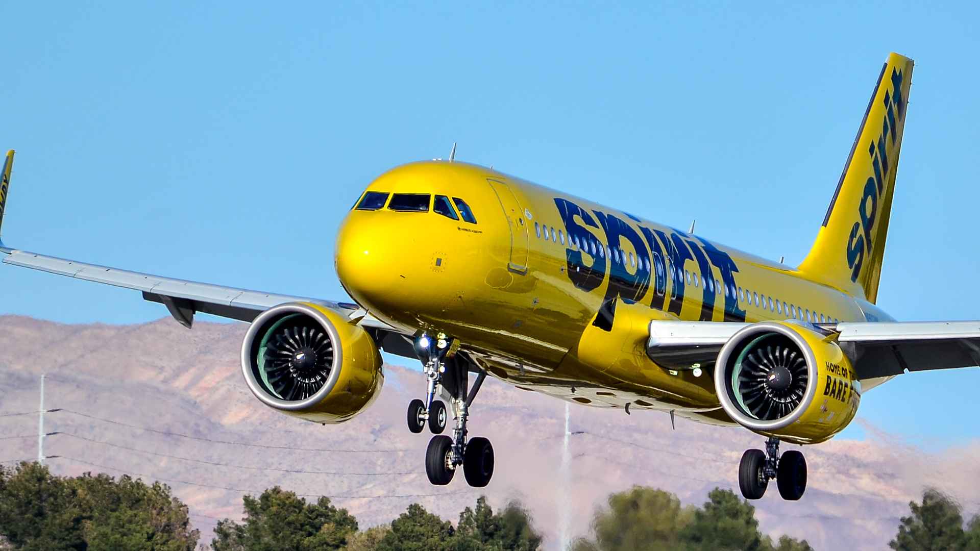 Spirit Airlines Airbus A320 in bright yellow livery landing against a desert backdrop, landing gear fully deployed