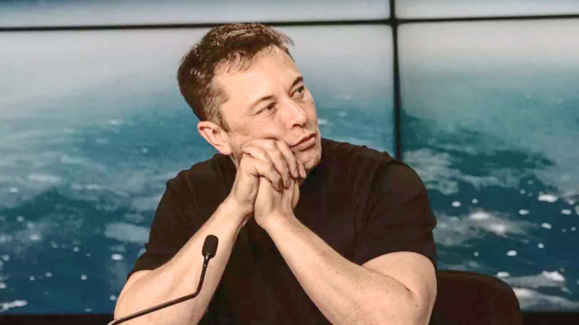 Contemplative automotive executive with clasped hands at press briefing amid concerns over Tesla’s declining sales and profit slump