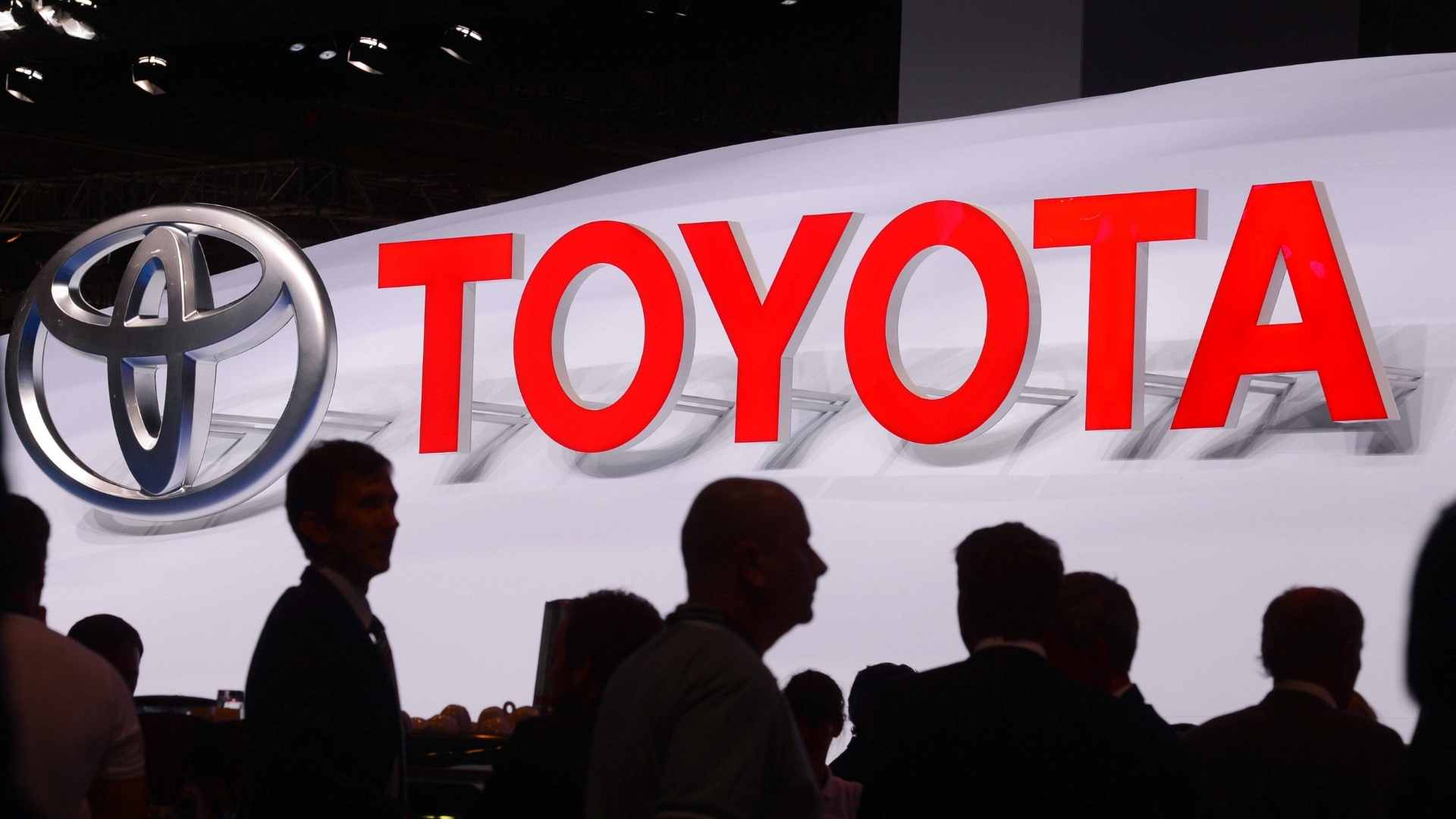 Toyota logo displayed at a press event announcing recall of over 100,000 Tundra and Lexus LX vehicles for 3.4-liter V6 engine defects
