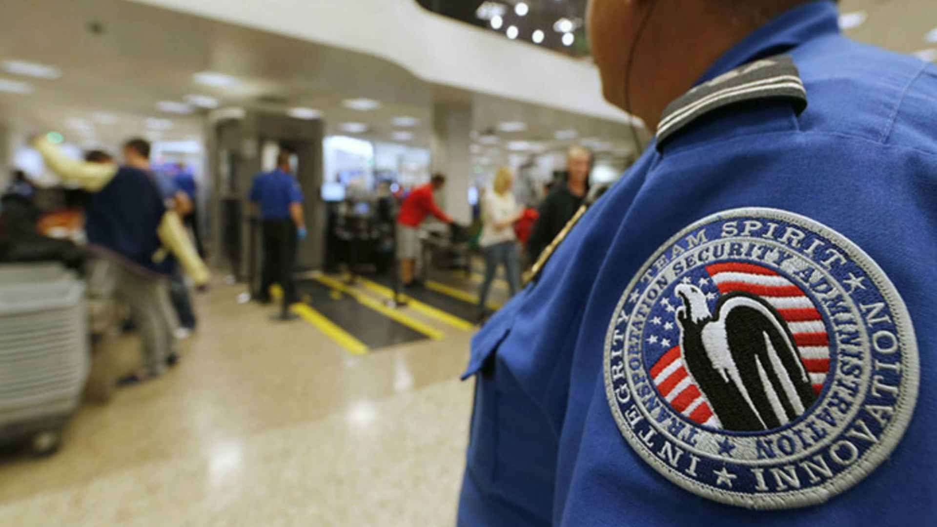 TSA officer stands by airport security lane enforcing new ban on power banks in checked luggage as travelers pass through screening.