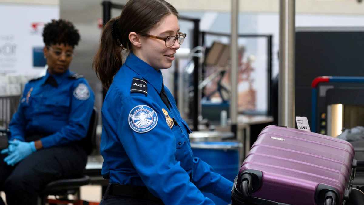 TSA officer inspects suitcase at airport after power bank ban on checked baggage
