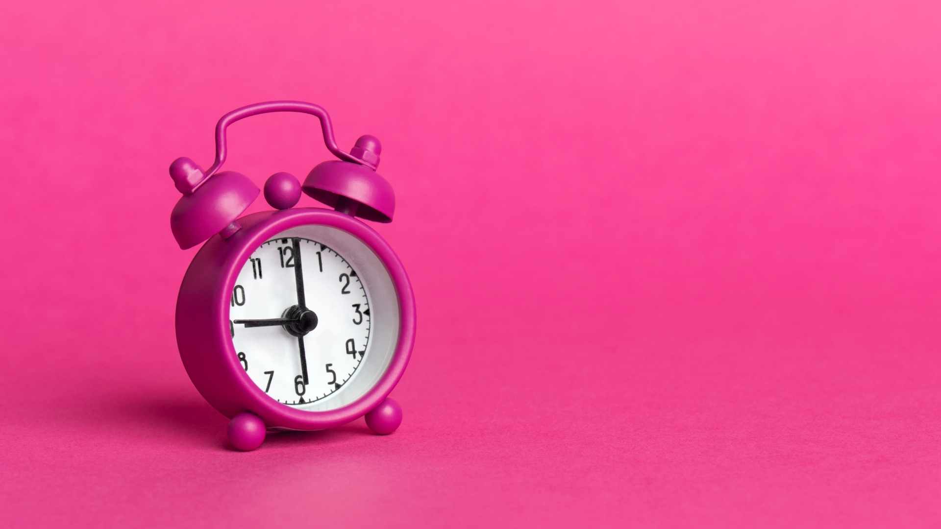 bright pink alarm clock on a monochrome pink background symbolizing the United States turning back the clocks for the end of daylight saving time 2025