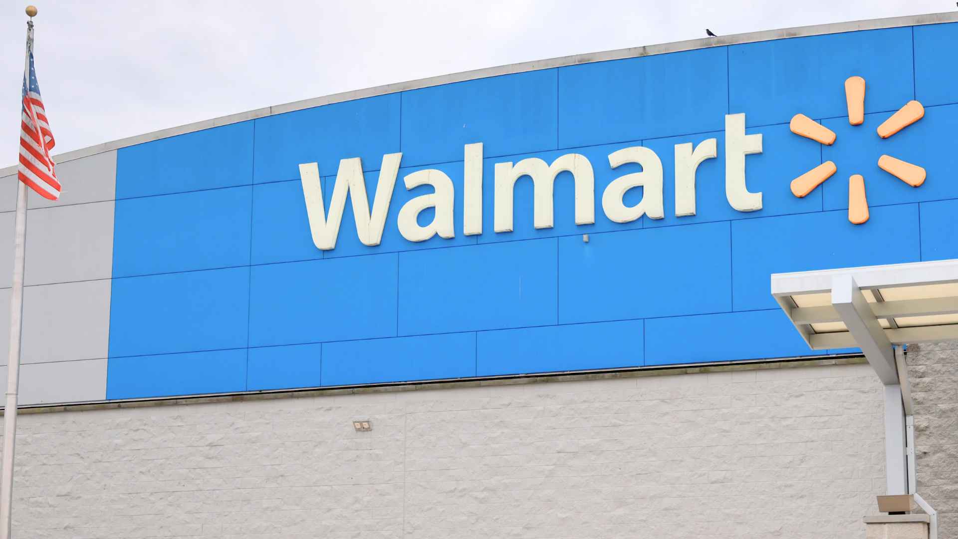 Exterior view of a Walmart store with large blue “Walmart” sign and an American flag flying beside the building.