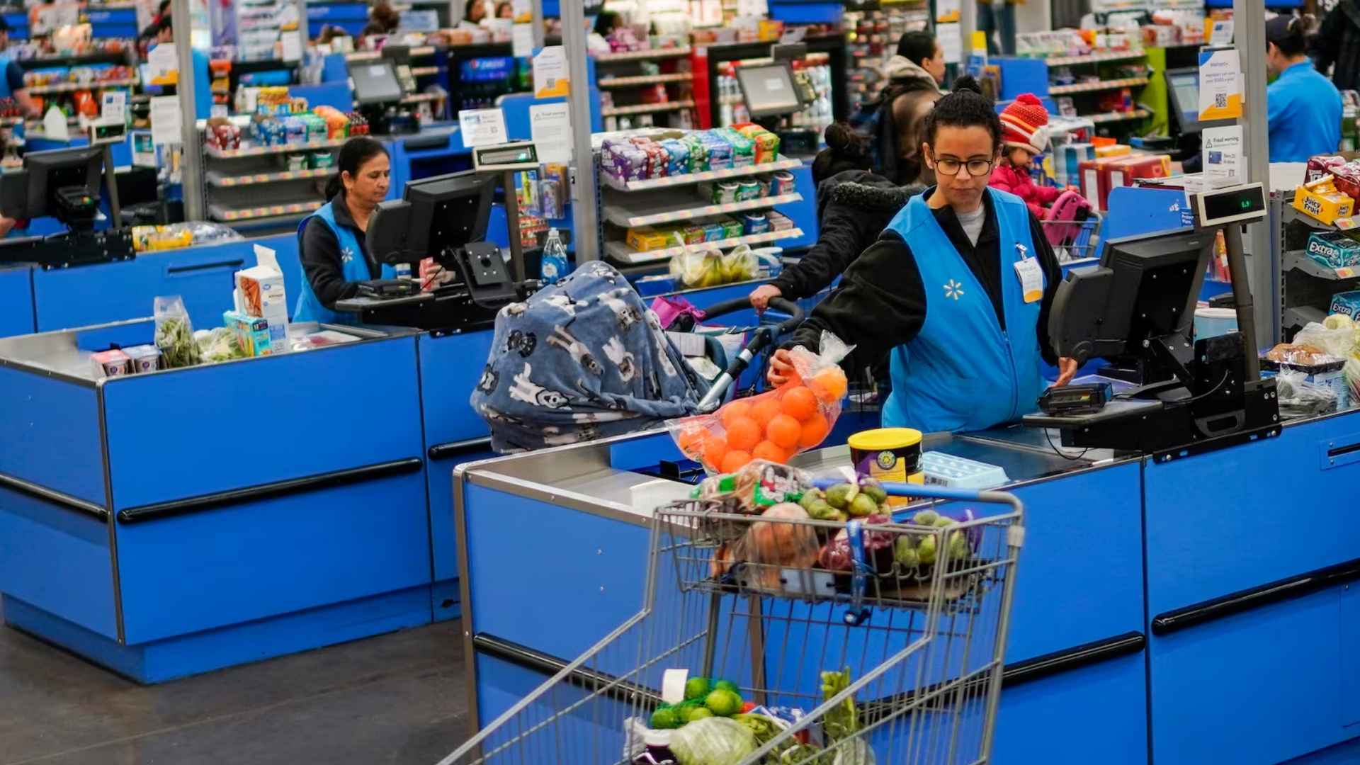 Walmart associate scans a bag of oranges and other groceries at a busy checkout lane
