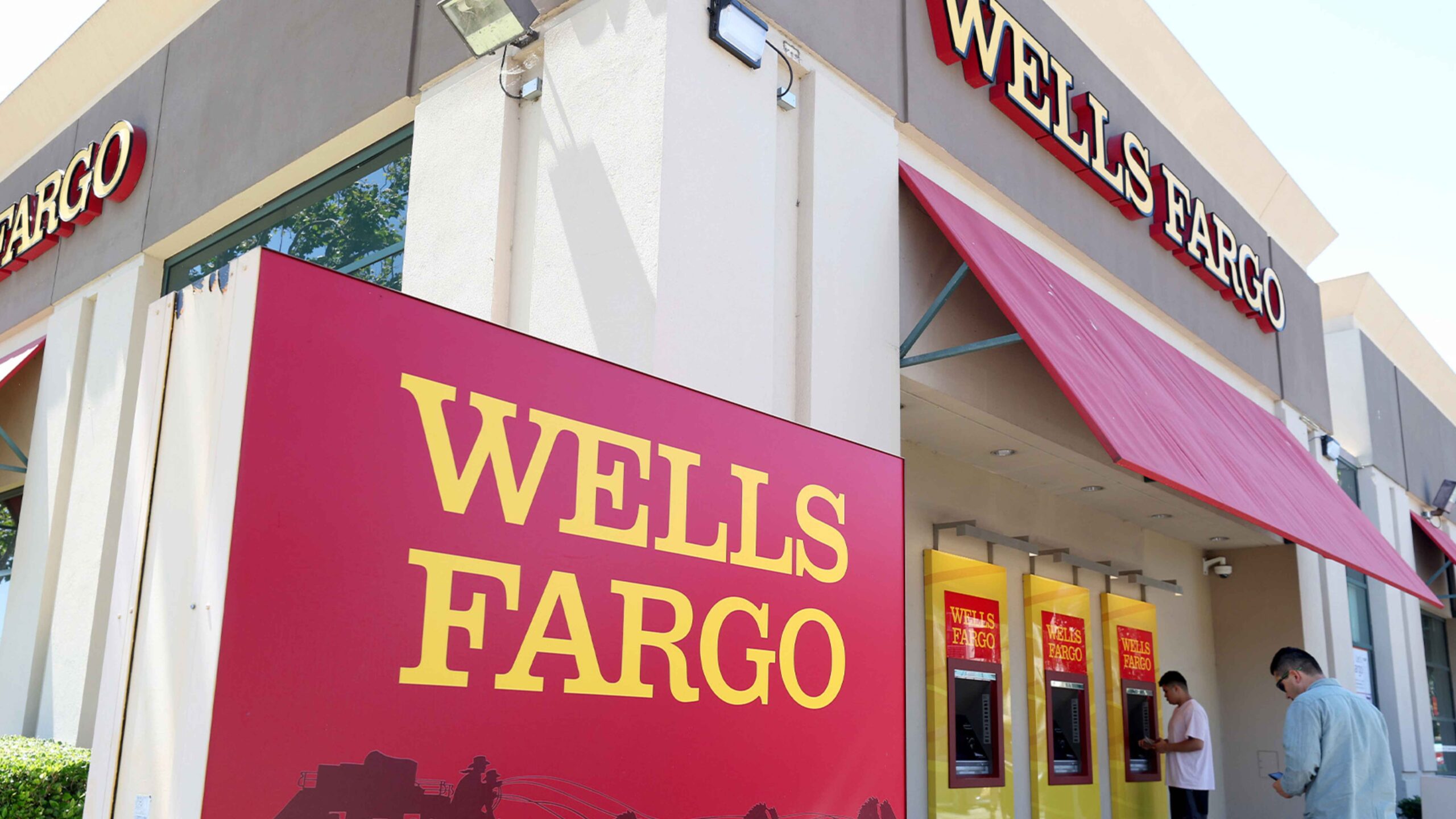 Exterior of a Wells Fargo branch with customers at ATMs, illustrating new digital-transfer conditions effective May 22 2025
