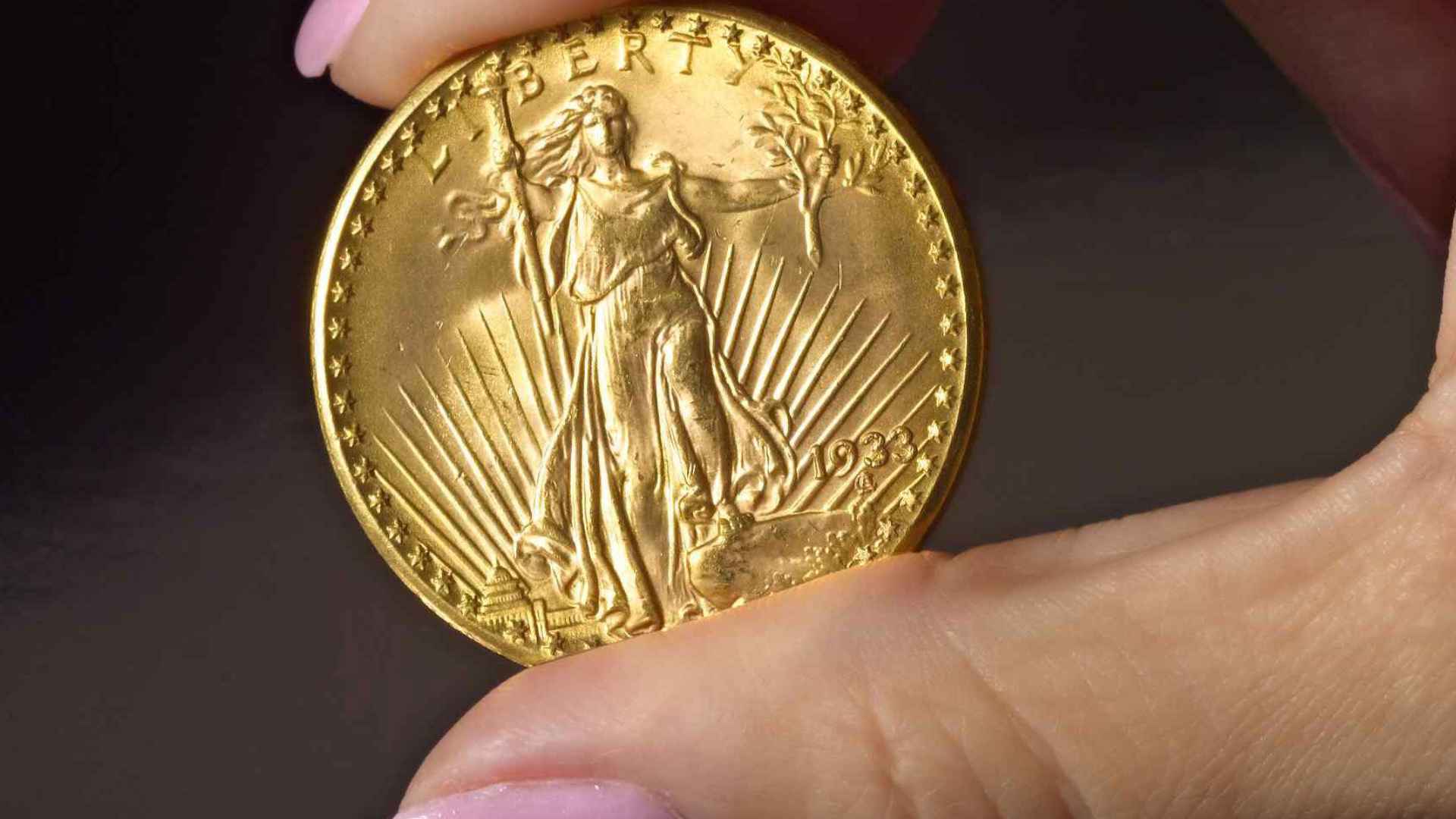 Rare 1933 Double Eagle gold coin held between fingers, valued at $19 million, discovered in Pennsylvania family safe.