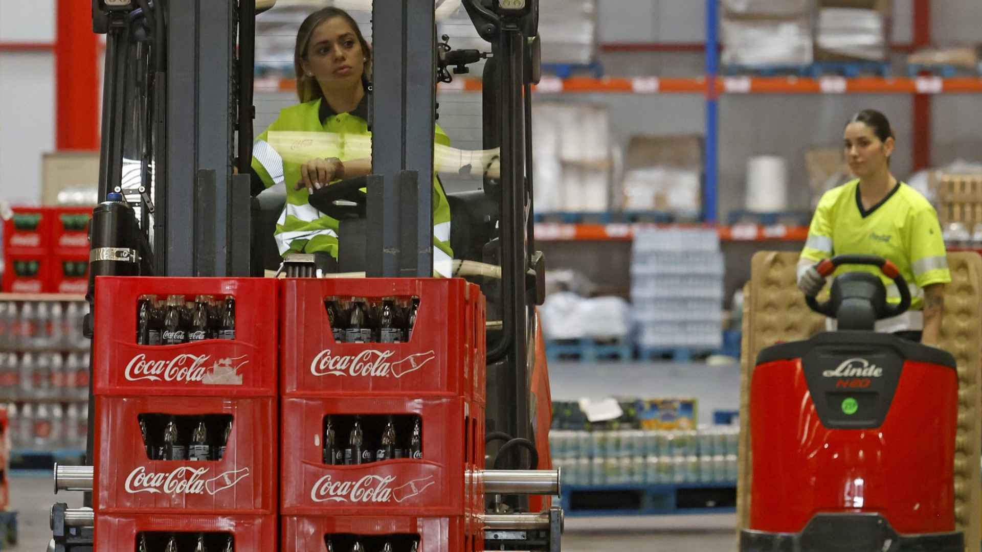 Warehouse workers maneuver stacked Coca-Cola glass-bottle crates with a forklift inside a distribution center during a recall for possible contamination.