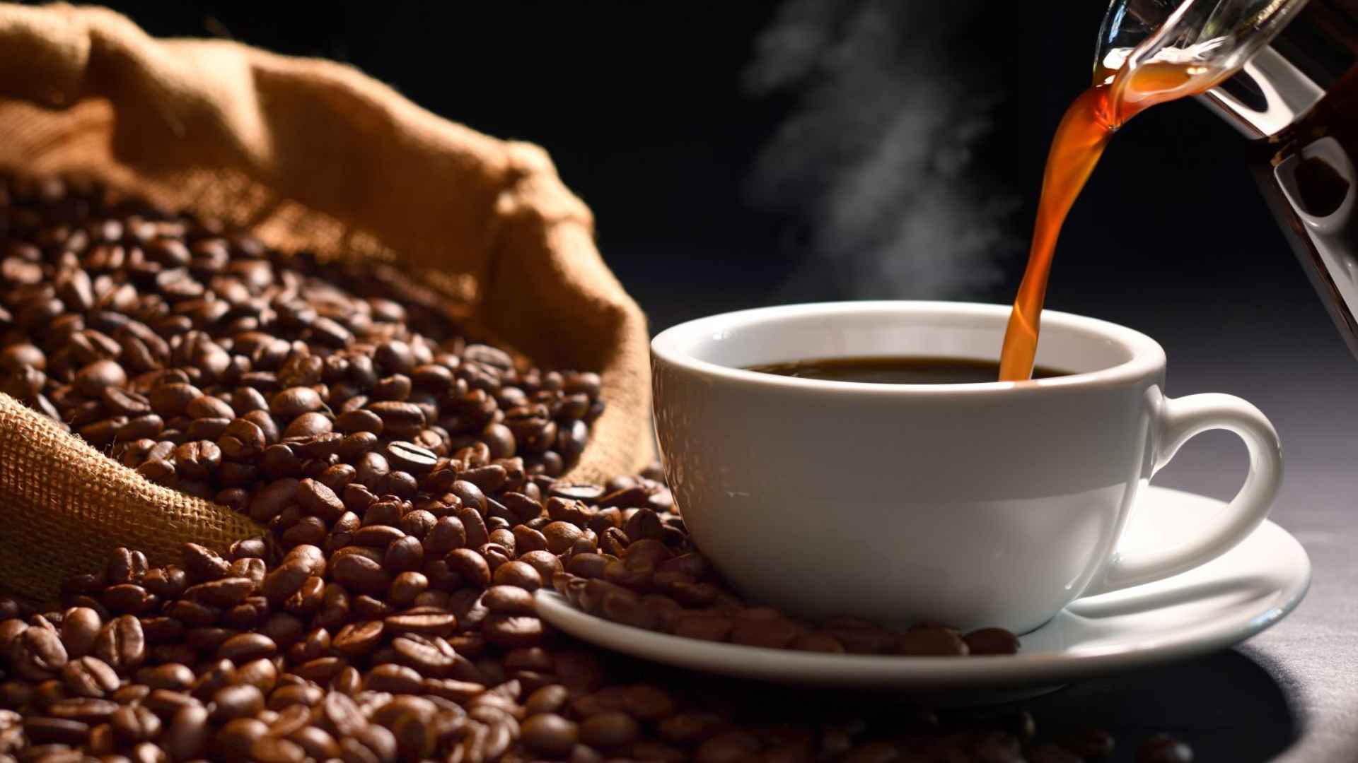 Steaming coffee pours into a white cup beside roasted beans as Nevada, California, and Arizona health officials warn caffeine worsens dehydration during extreme heat.
