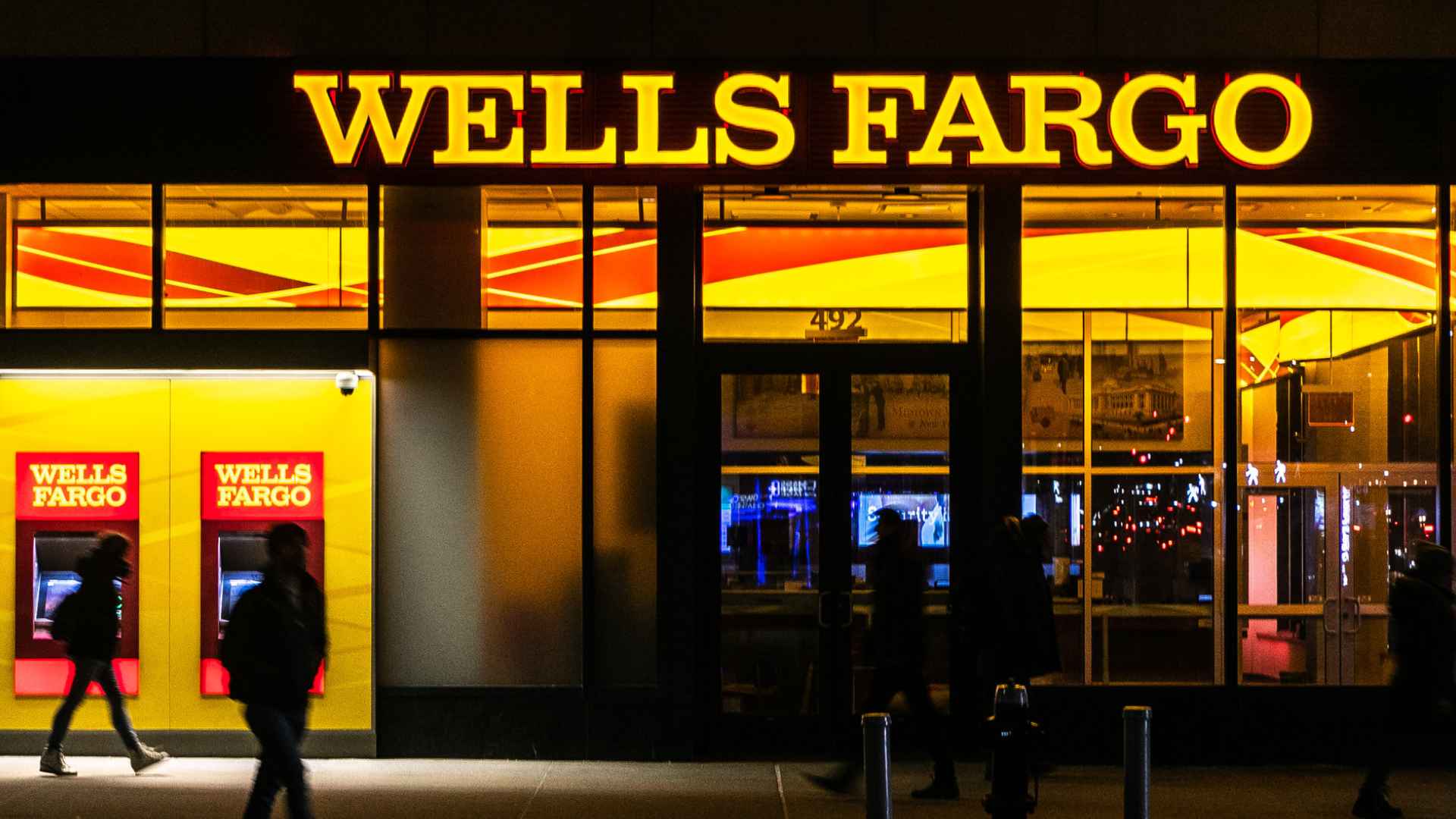 Wells Fargo branch storefront at night with illuminated signage and ATMs