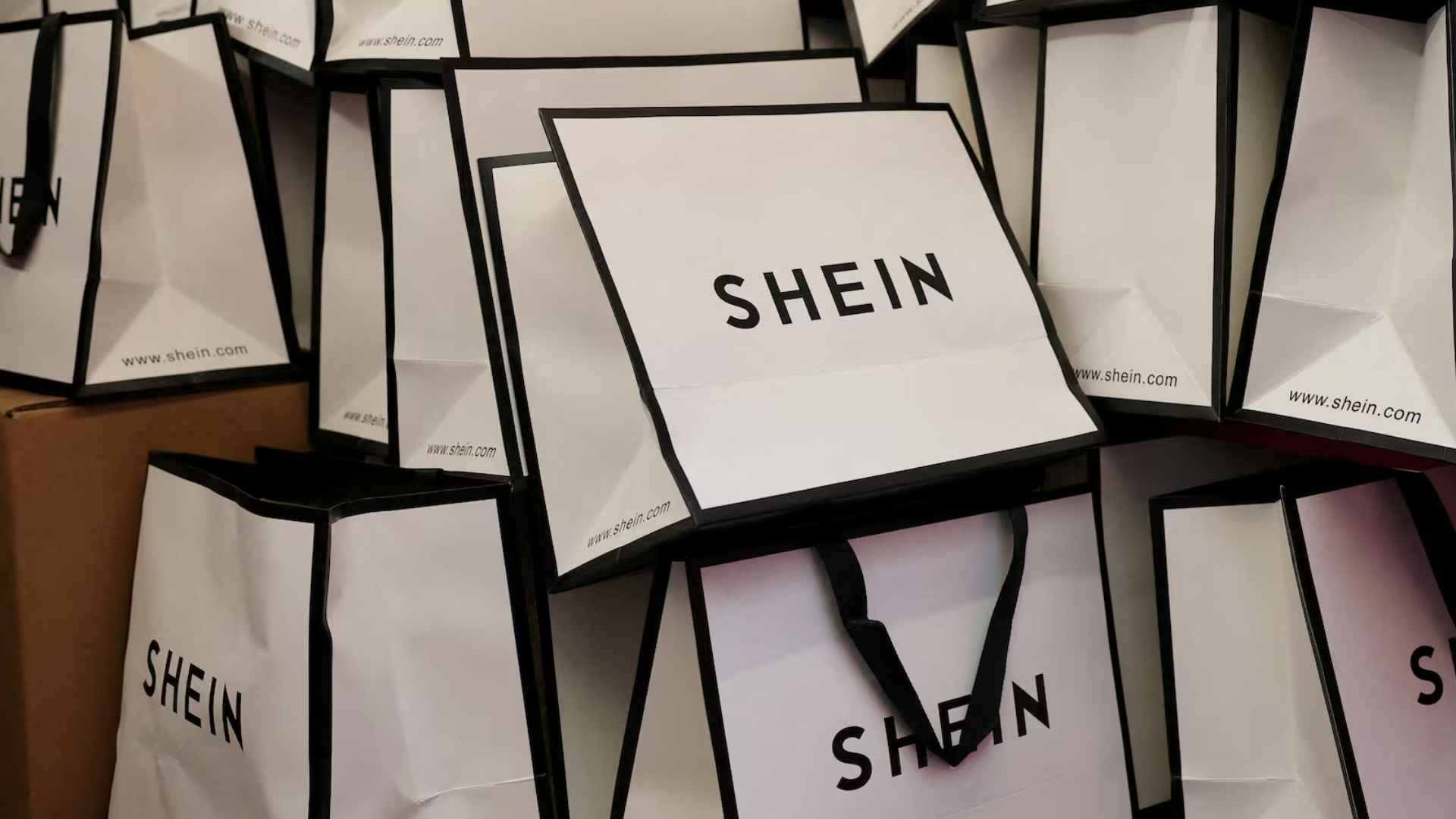 Stack of white Shein shopping bags piled on cardboard boxes inside a store display.