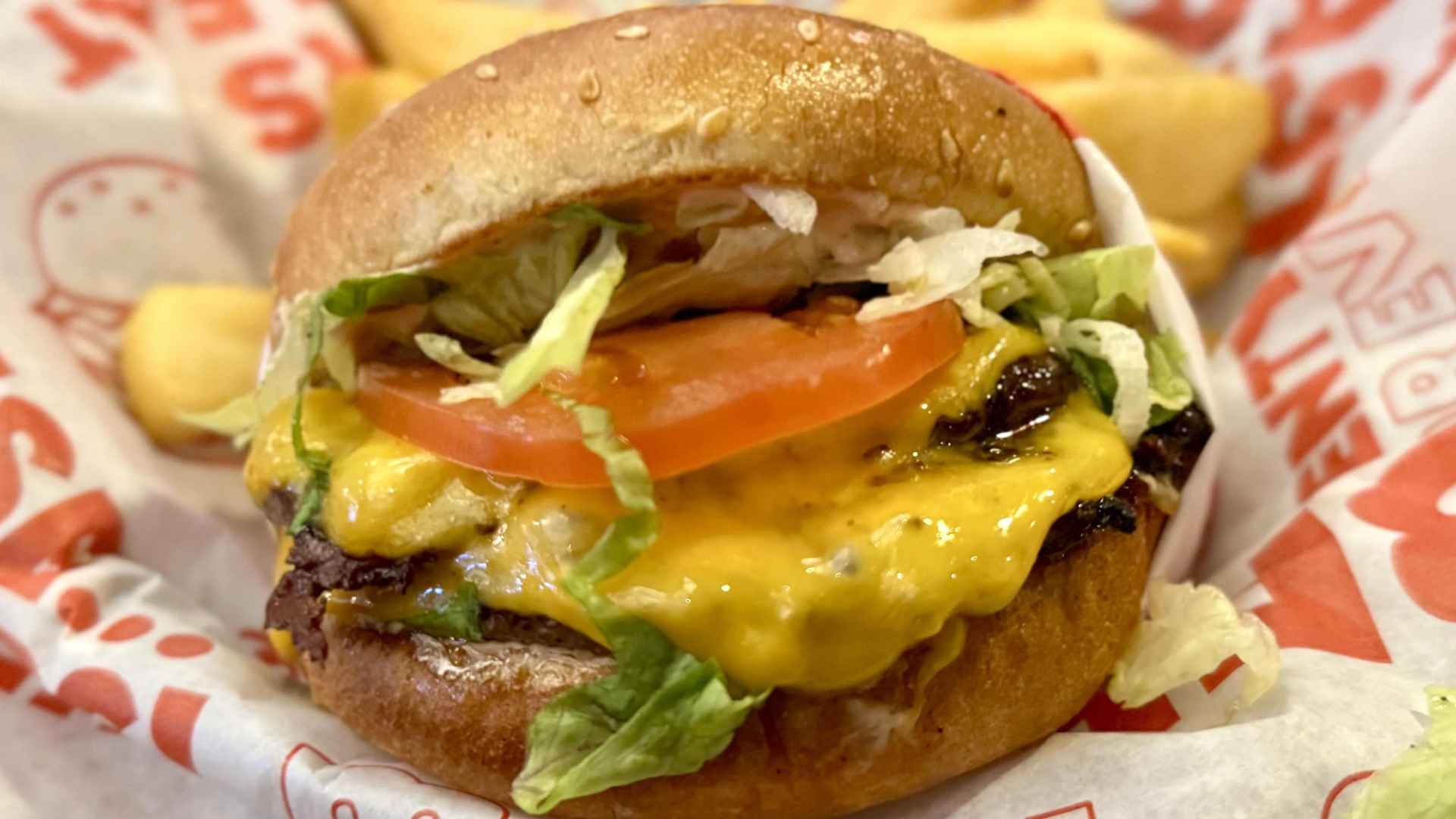 Close-up of a Red Robin signature cheeseburger slider with melted cheese, lettuce, tomato and fries on a branded paper wrapper.