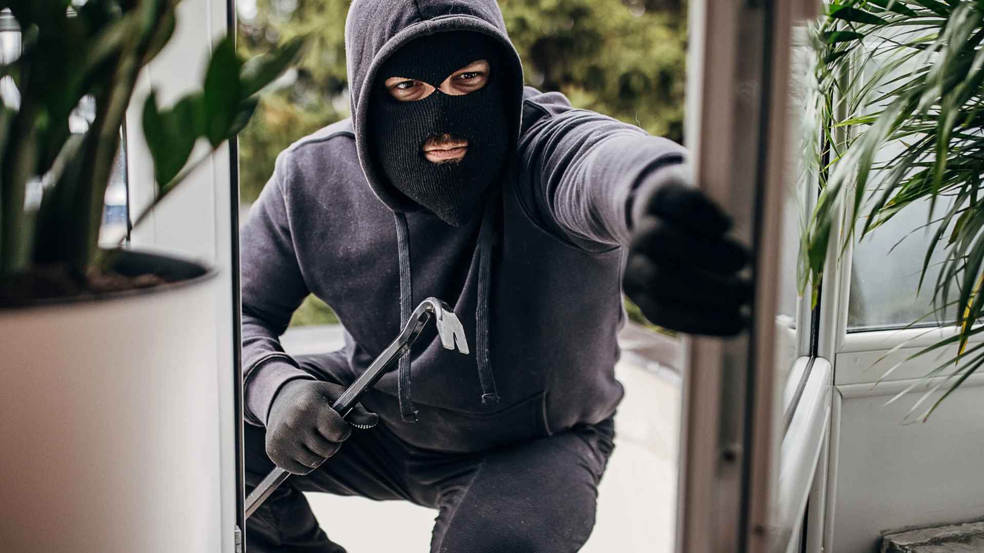 Masked burglar breaking into home through door with crowbar during vacation season