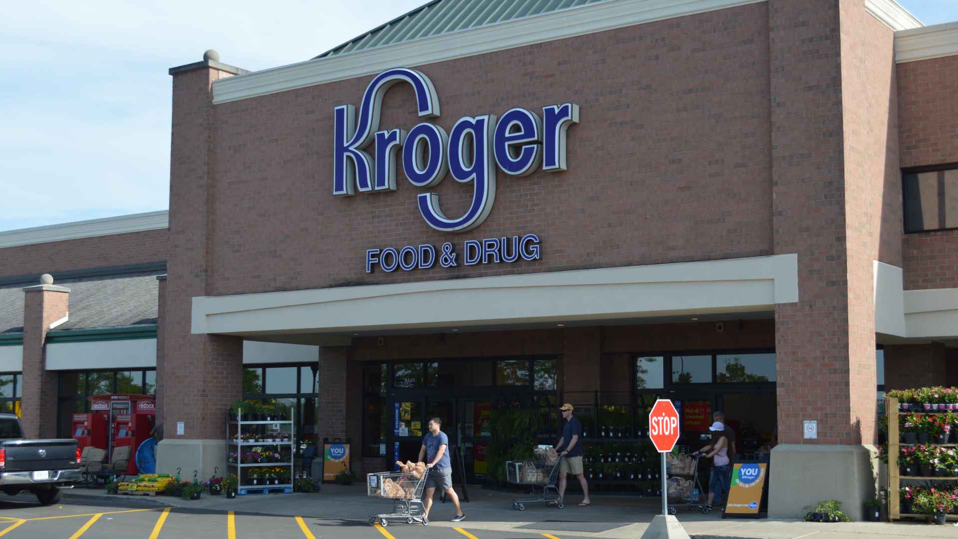 Customers pushing shopping carts outside a Kroger Food & Drug storefront in a parking lot.