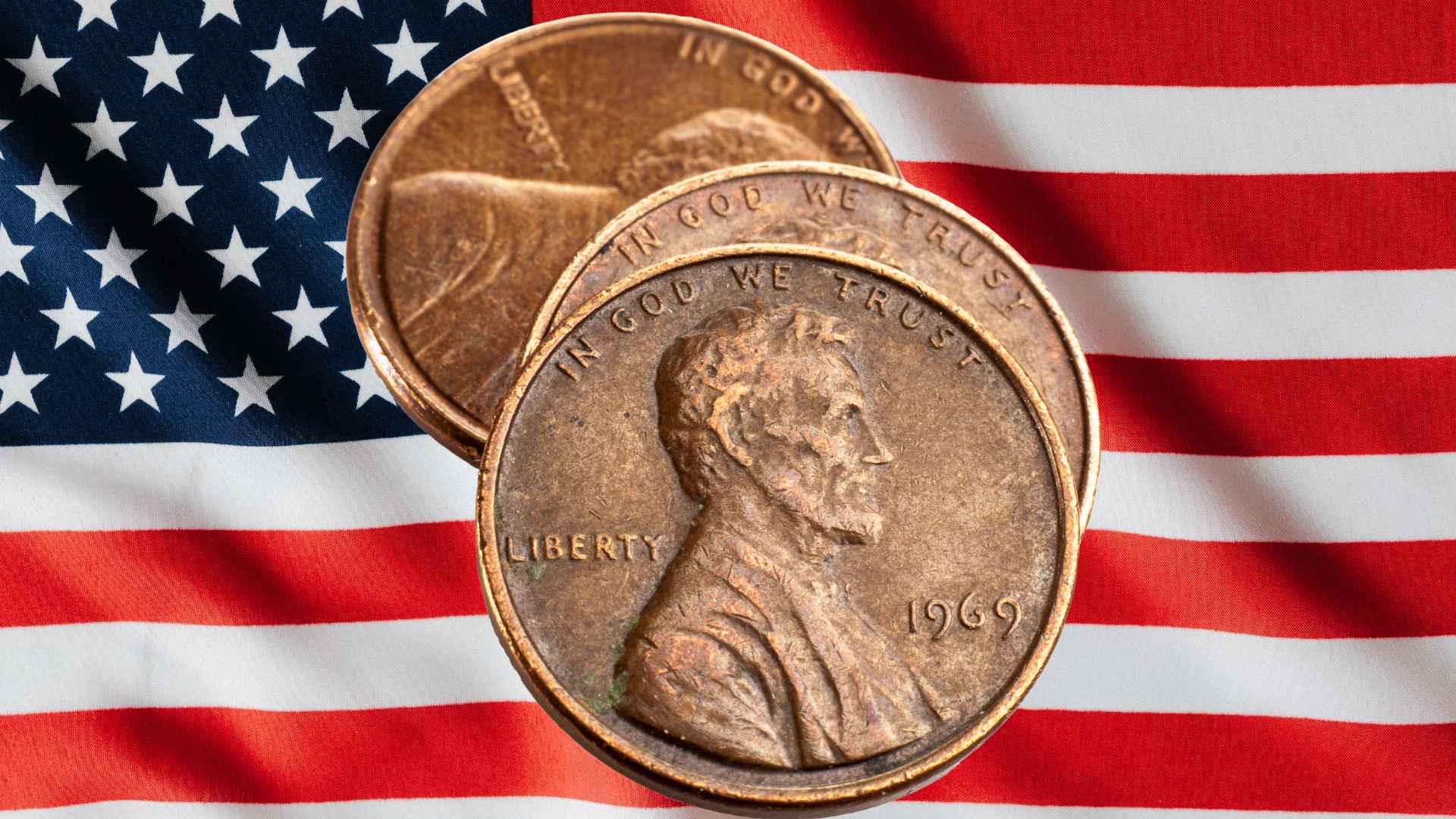 Close-up of three worn Lincoln pennies on a waving American flag, illustrating the U.S. penny’s retirement after 230 years.