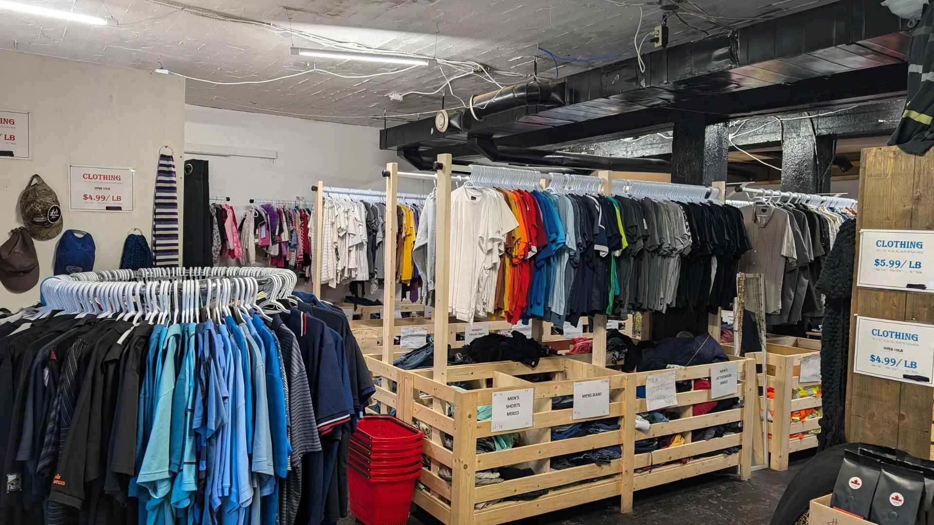Rows of secondhand clothing in a thrift store with racks and bins labeled by price per pound
