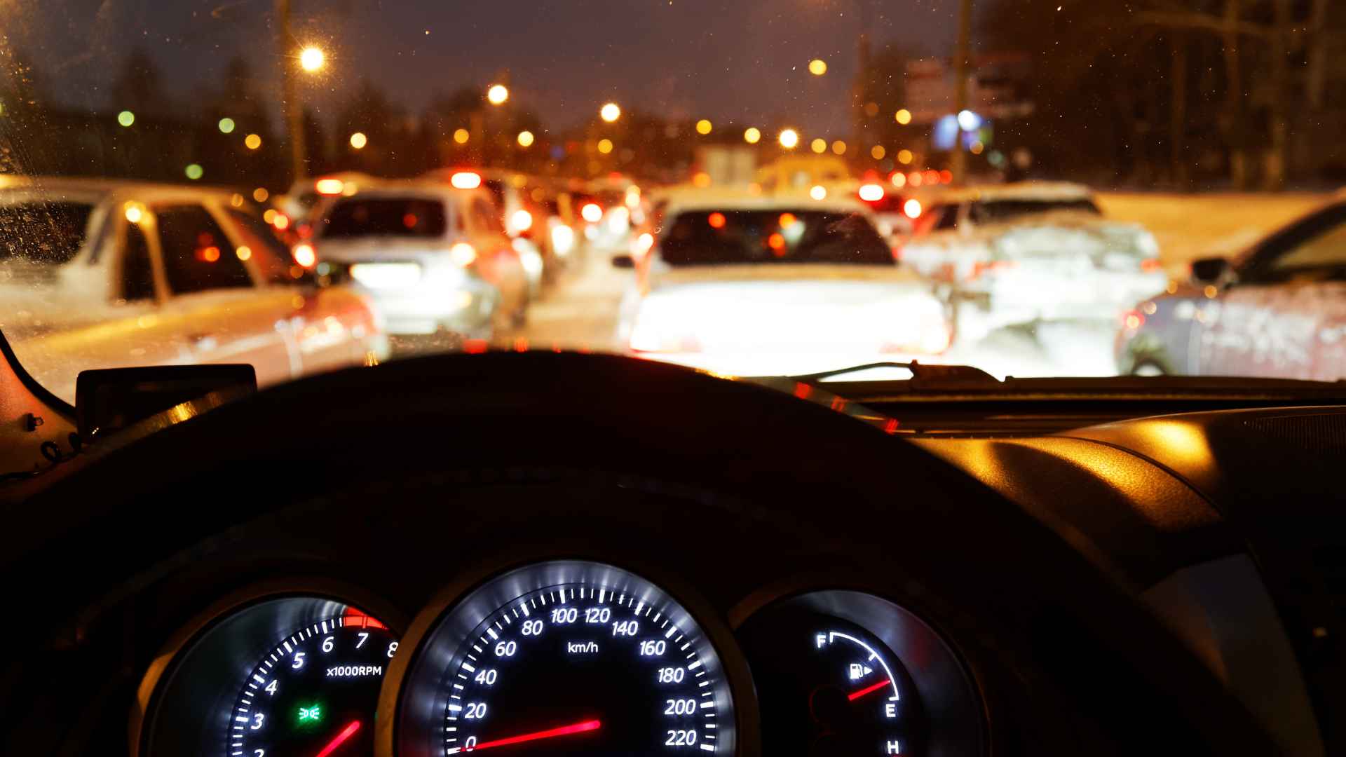 Night traffic seen from a driver’s seat in New York, dashboard gauges lit, illustrating the 2025 headlight law that fines motorists who forget their lights