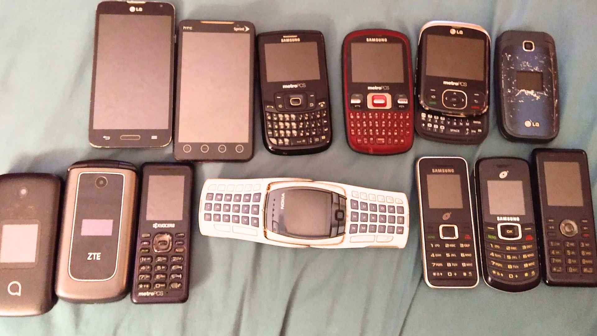 Collection of old cell phones including flip phones, sliders, and early smartphones arranged on a surface