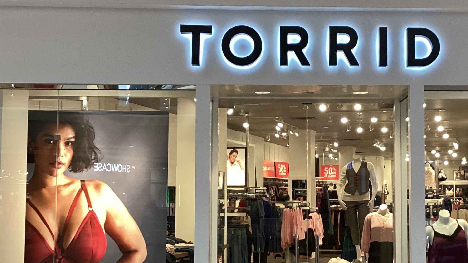 Torrid store entrance with glowing logo and plus-size model poster ahead of nationwide store closures