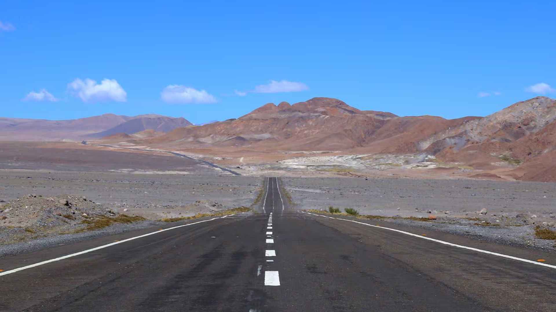 Straight two-lane stretch of Nevada’s US Route 50—the “Loneliest Road”—cutting across empty high desert beneath a cloudless blue sky.