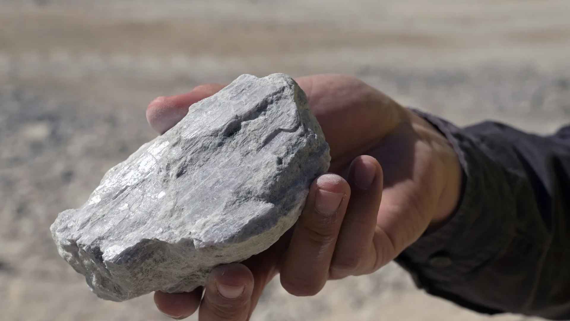 Hand of a geologist holding gray lithium-rich rock sample from Arkansas’s newly discovered 19-million-ton deposit.