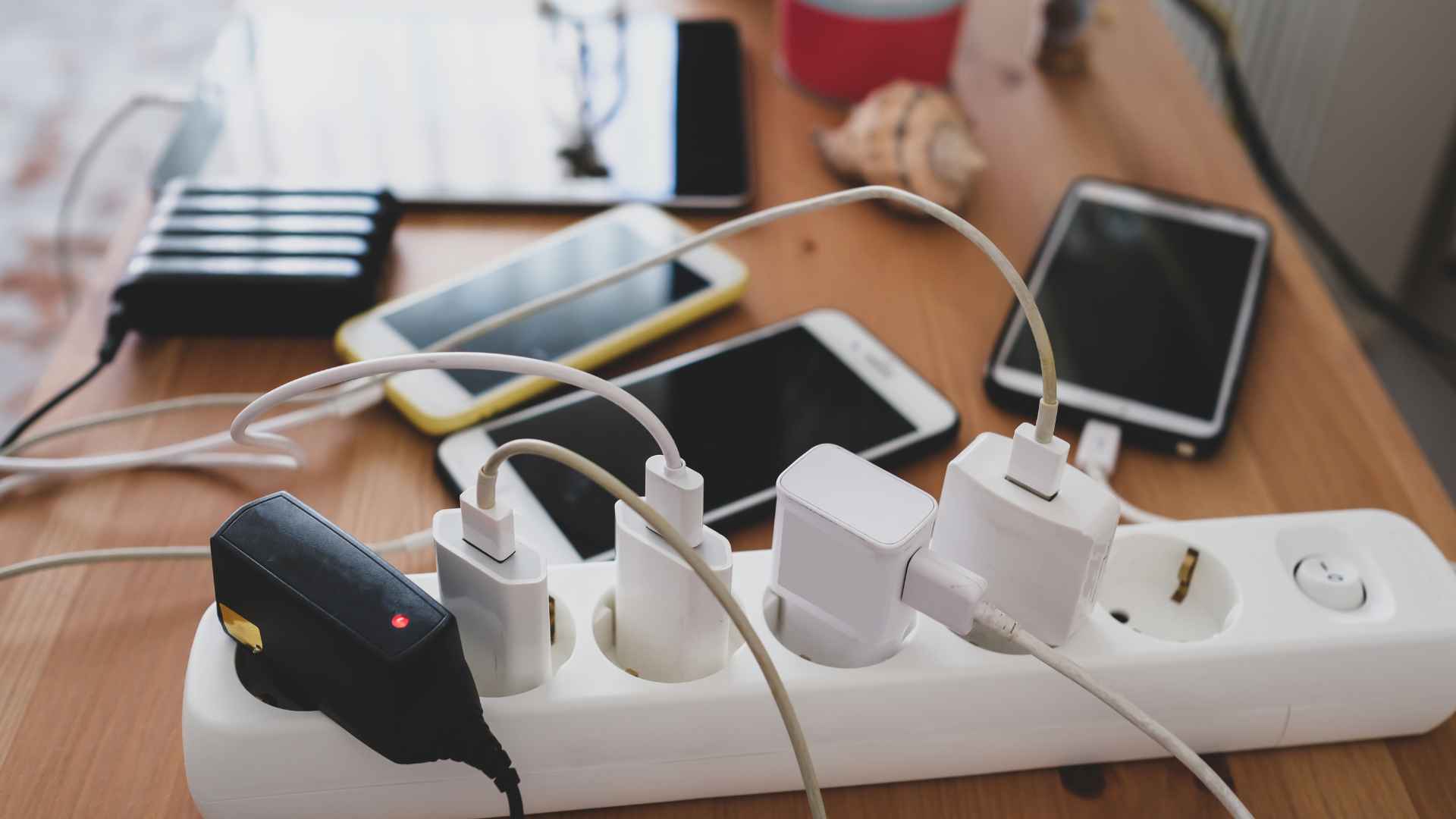 Multiple phone and tablet chargers plugged into a power strip on a wooden table