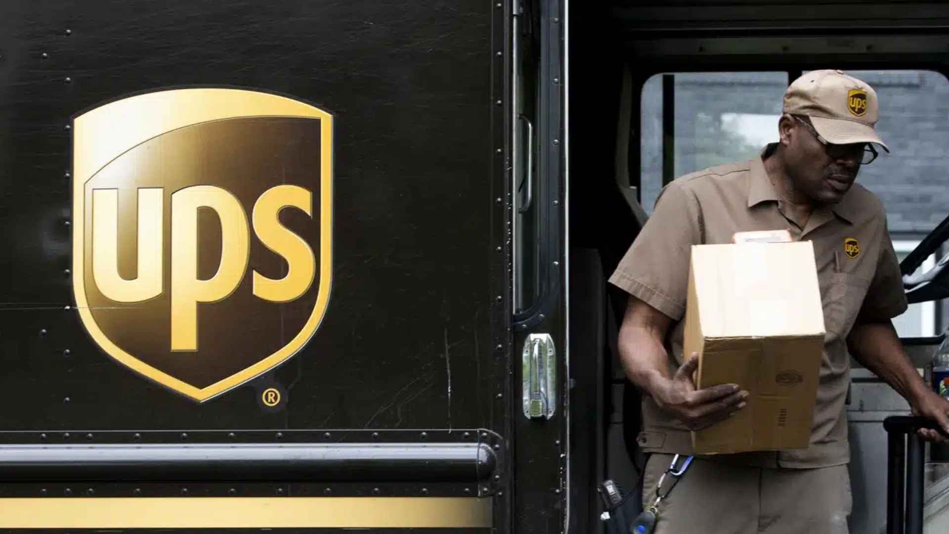 UPS driver holding a cardboard box beside a brown UPS truck with company logo visible
