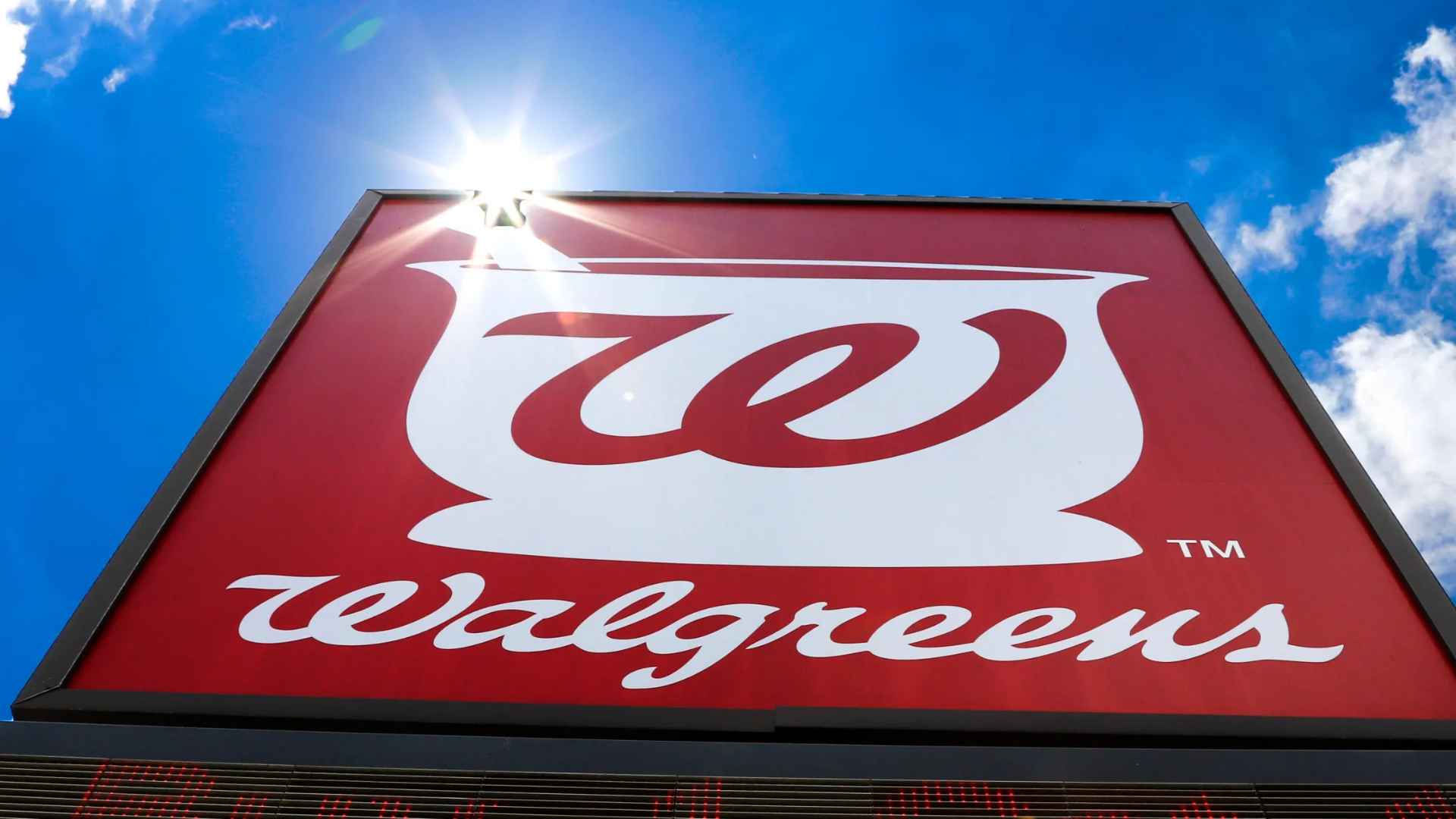 Walgreens red-and-white logo sign set against a bright blue sky outside a retail pharmacy.