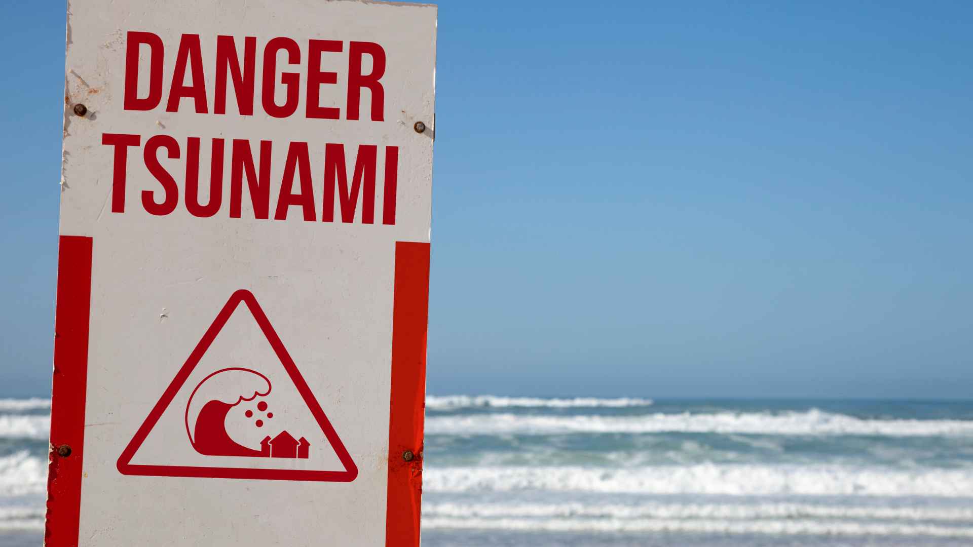 Tsunami warning sign posted on a beach with ocean waves in the background, symbolizing coastal threat