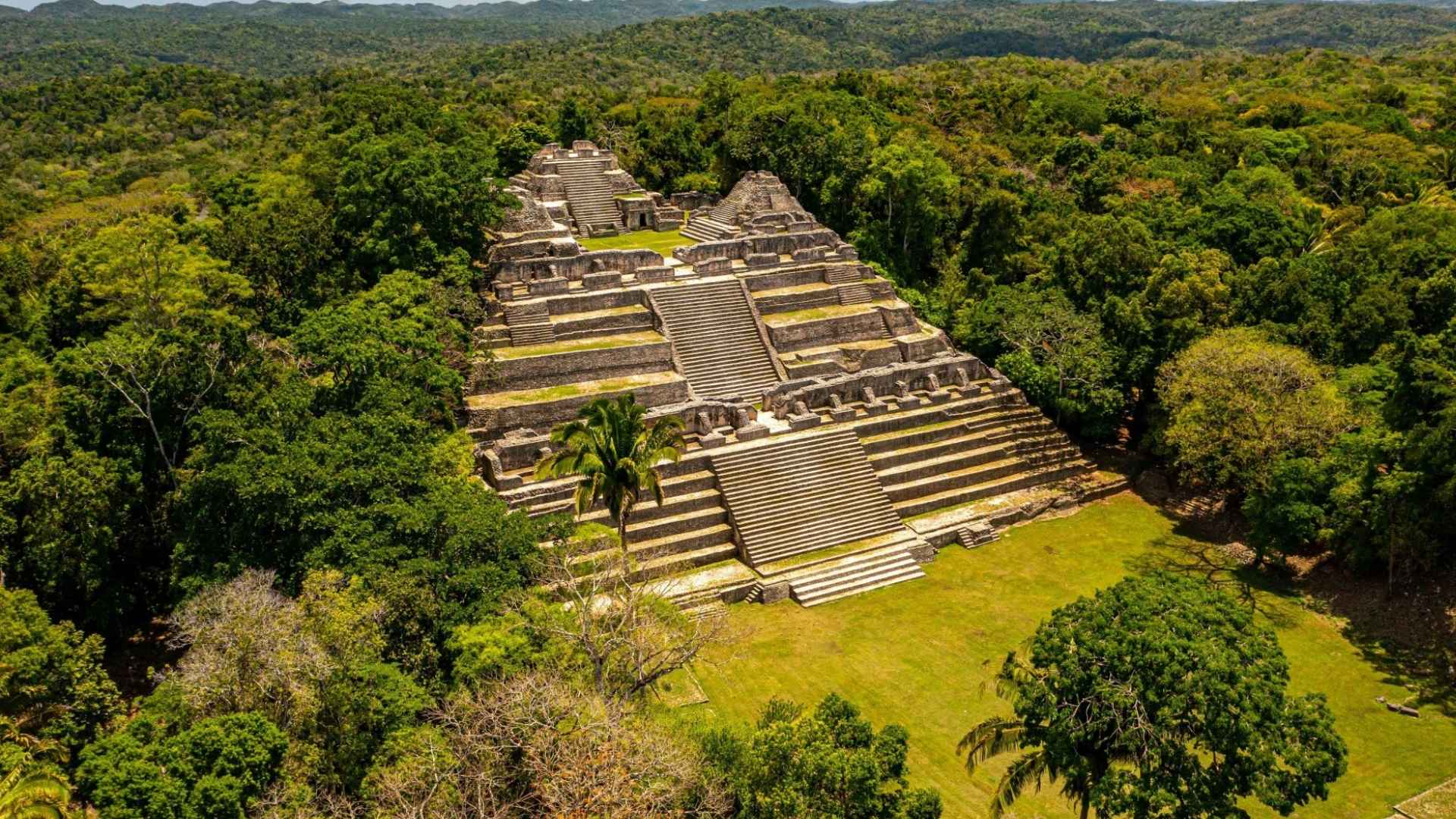 Aerial view of ancient Maya pyramids at the archaeological site of Caracol surrounded by dense Belize jungle.