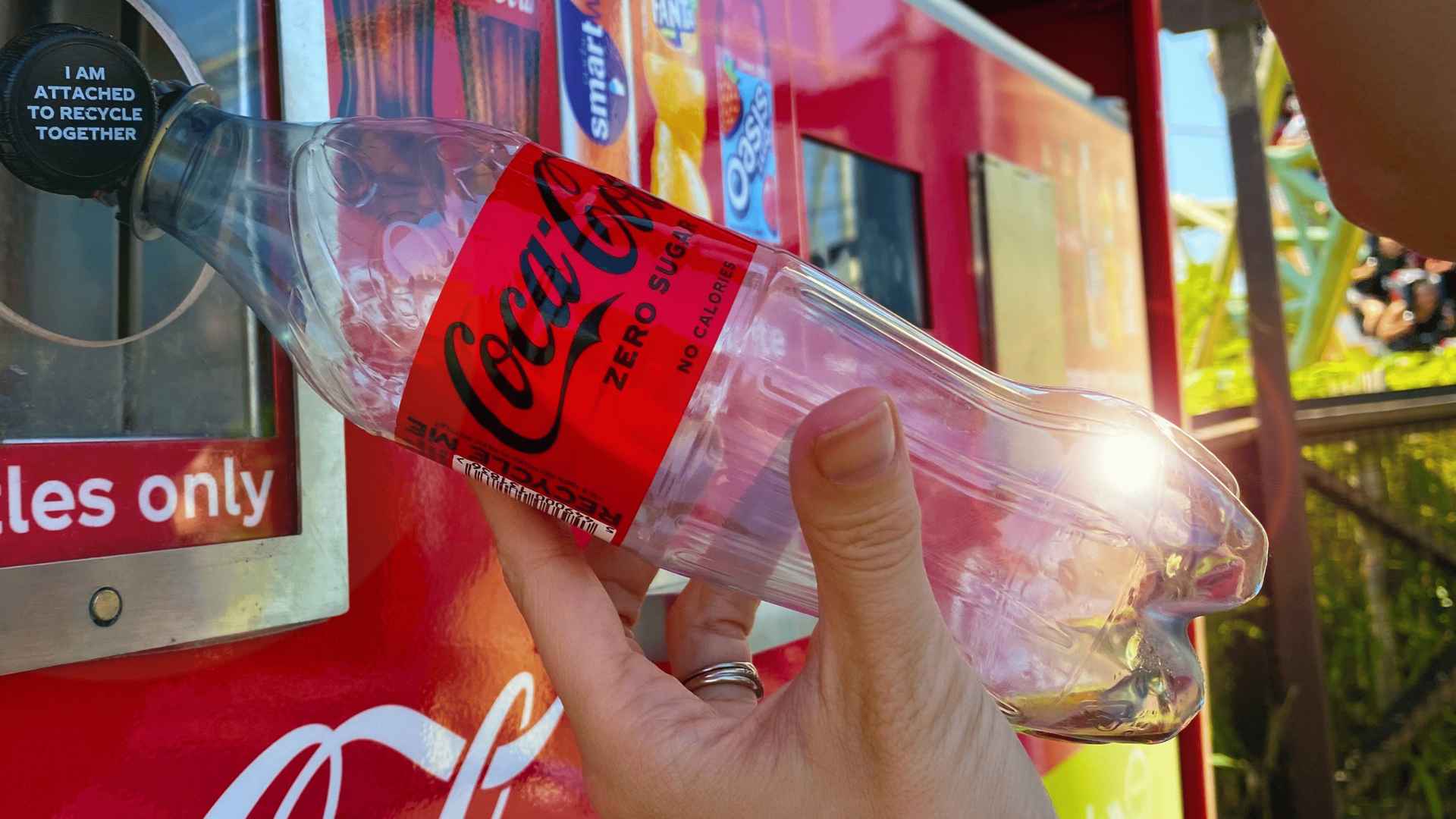 Person recycling a Coca-Cola bottle using a reverse vending machine designed to reward eco-friendly actions