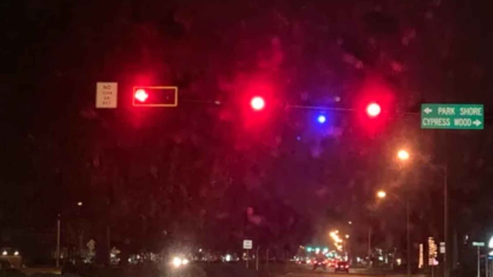 Traffic signal at night with mysterious blue confirmation light between two red lights in Florida intersection.