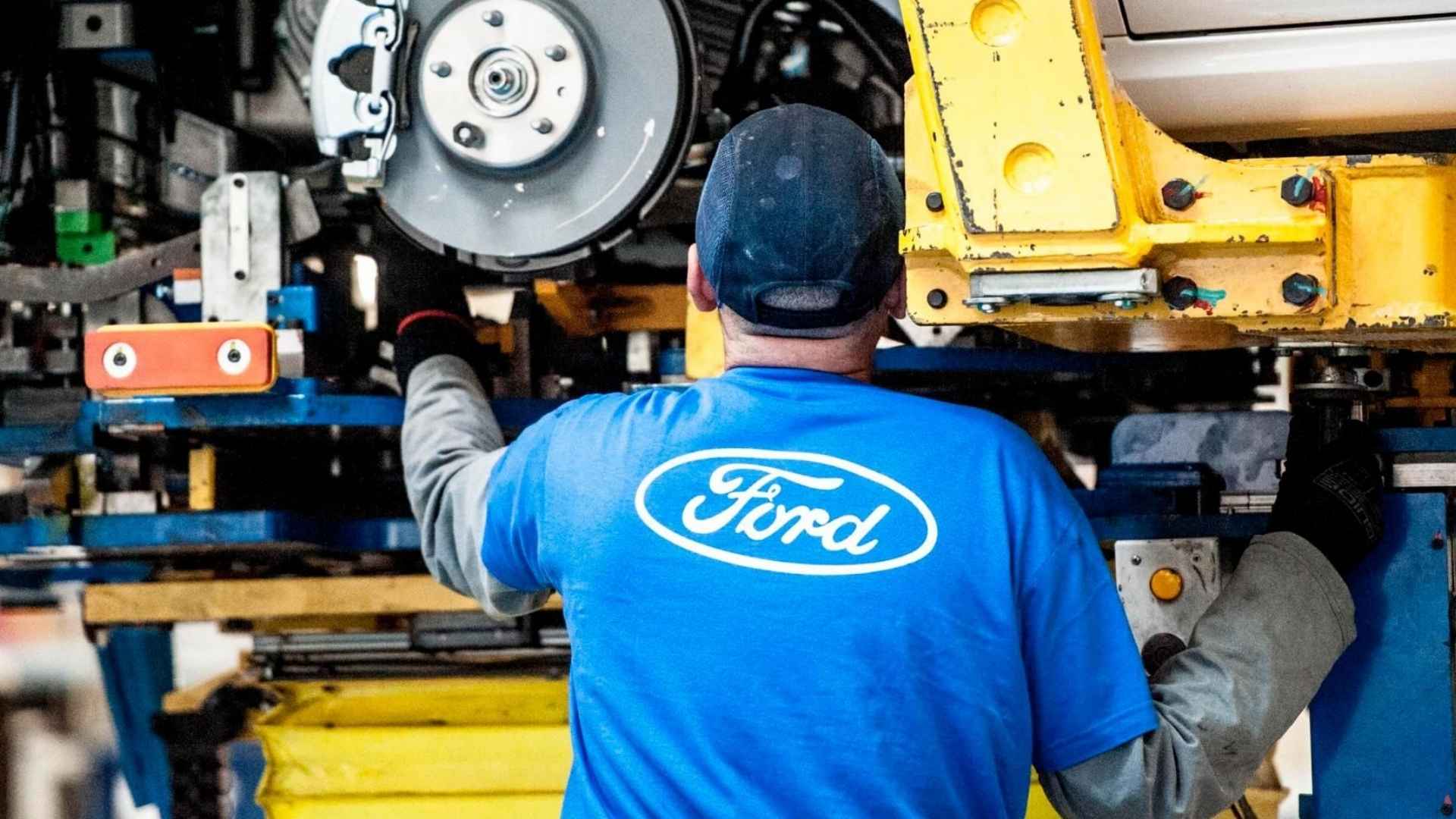 Ford factory worker inspects brake system on vehicle assembly line during safety recall operations.