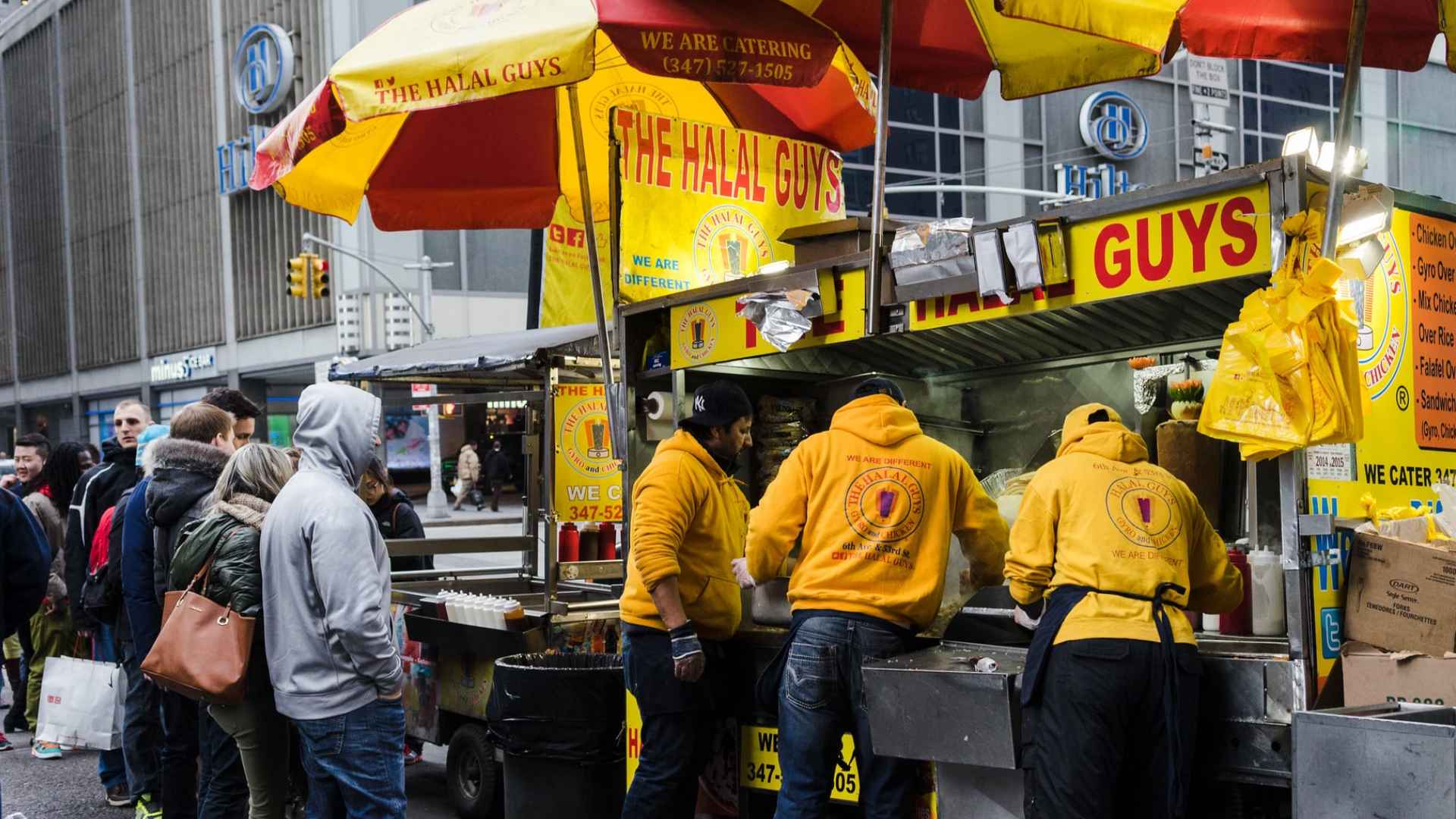 Crowd lining up at The Halal Guys food cart in Midtown Manhattan, illustrating the NYC street vendors decriminalized by Law 47.