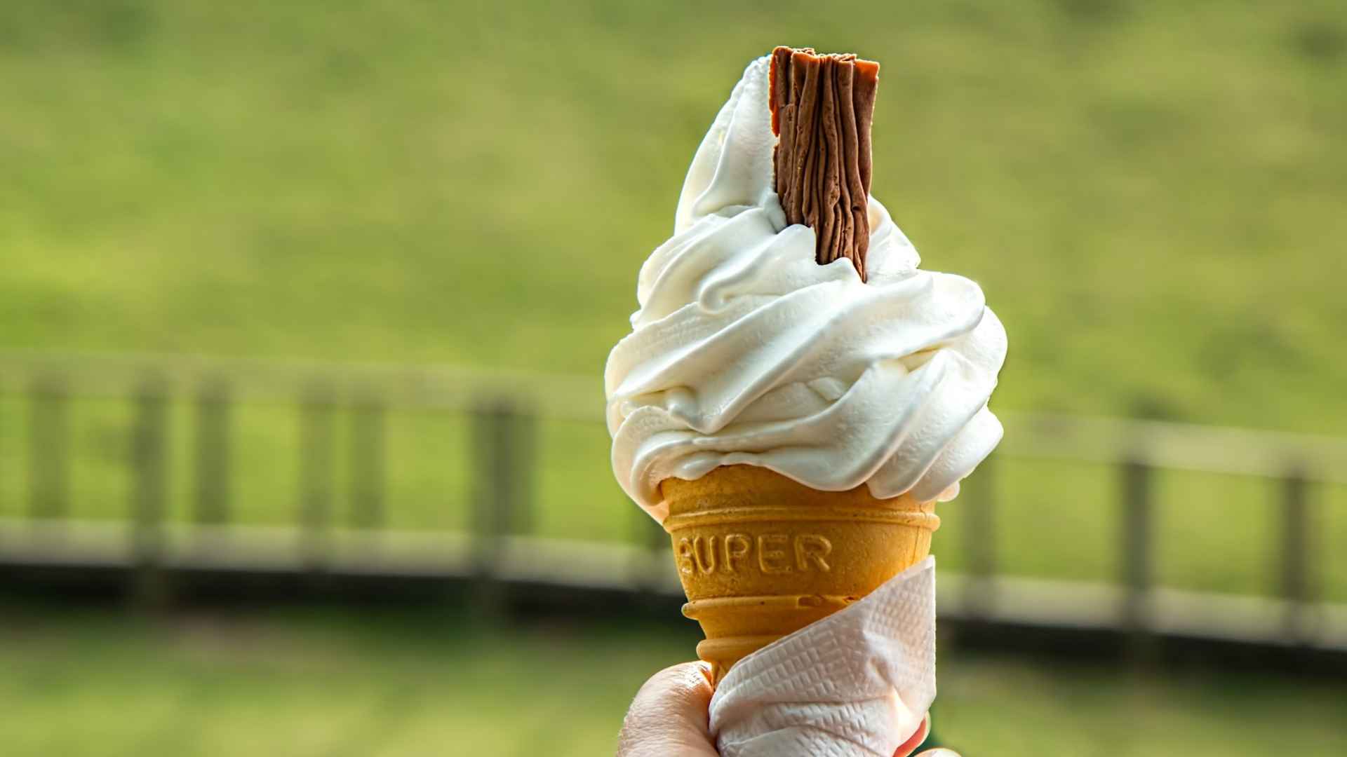 Hand holding a vanilla soft-serve ice cream cone topped with chocolate flake outdoors in Portland area.