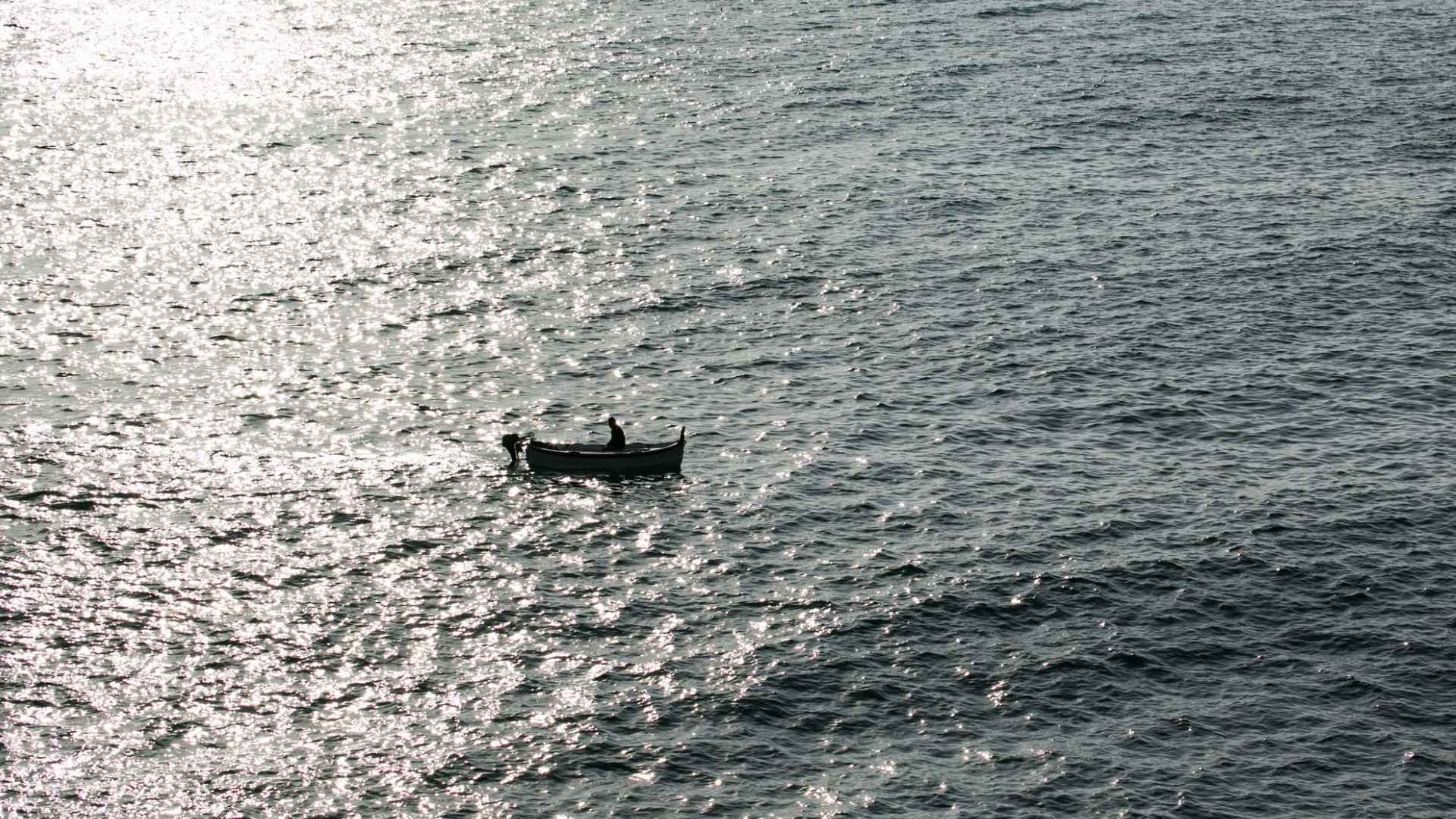 Stranded fisherman alone in small boat on vast Pacific Ocean under sunlight reflections