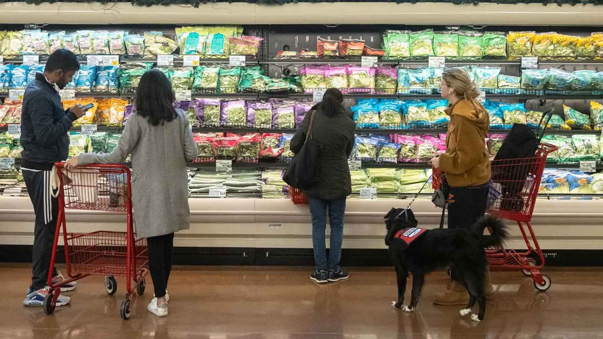 Customers browse bagged salads inside Trader Joe’s Sherman Oaks, Los Angeles, with red carts and a service dog nearby.