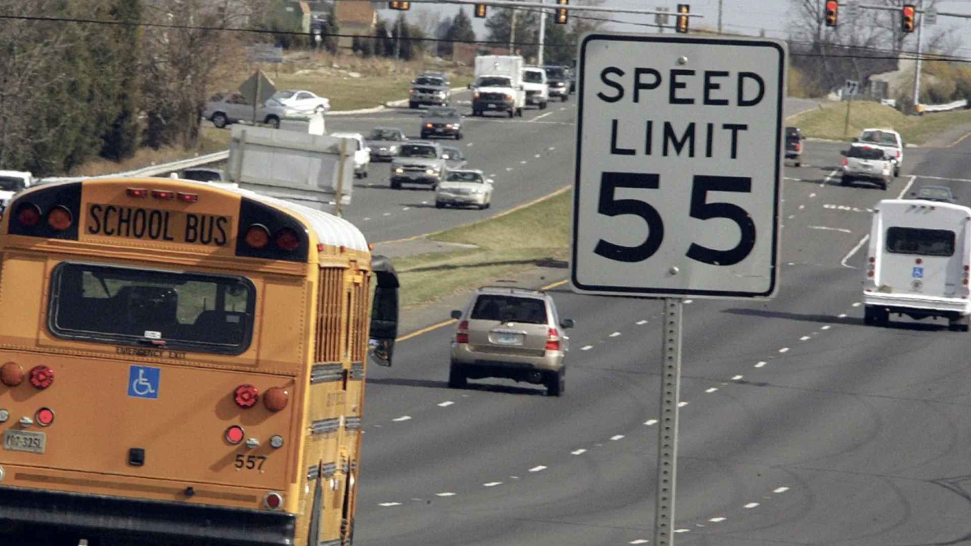 Virginia highway with a 55 mph speed-limit sign, school bus, and cars—visualizing the state’s new mandate for speed-limiting devices on reckless drivers’ vehicles.