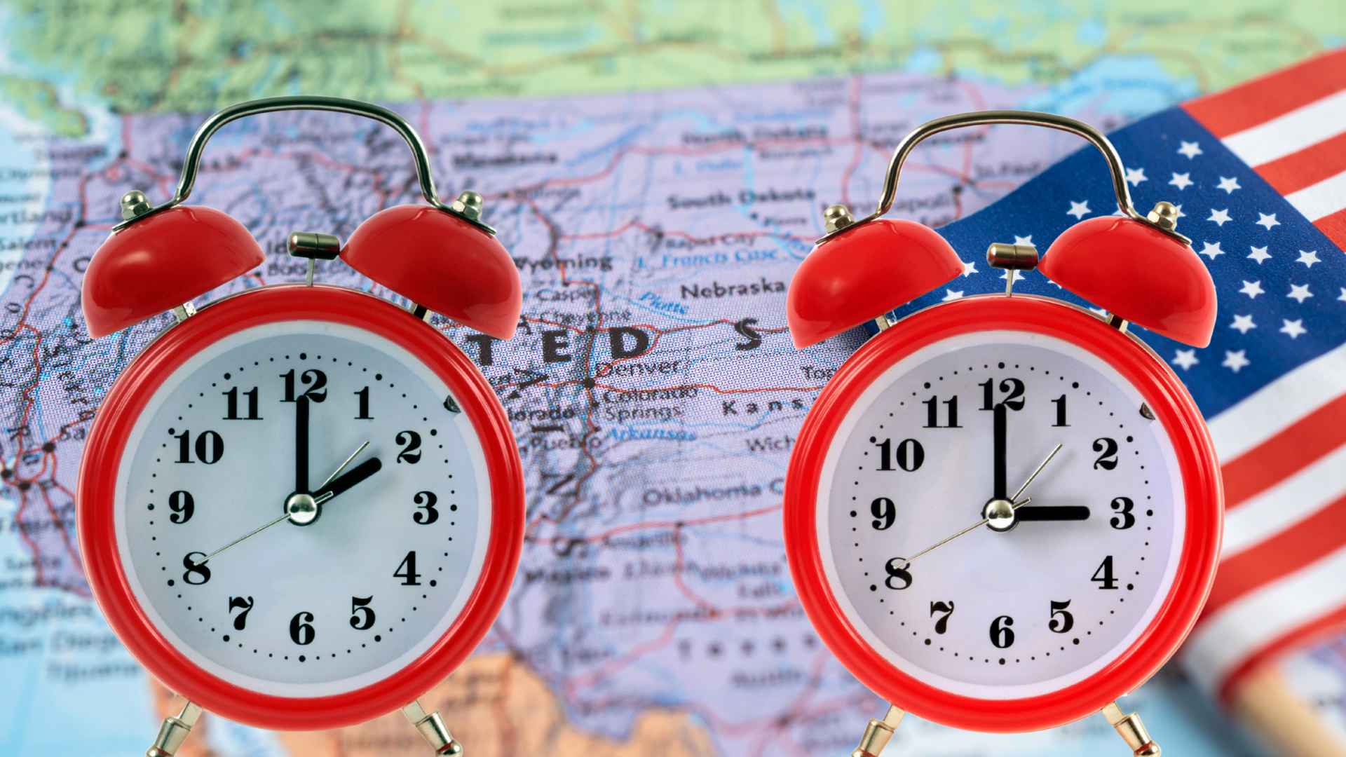 Two red alarm clocks showing different times placed on a map of the United States with an American flag, symbolizing the end of daylight saving time.