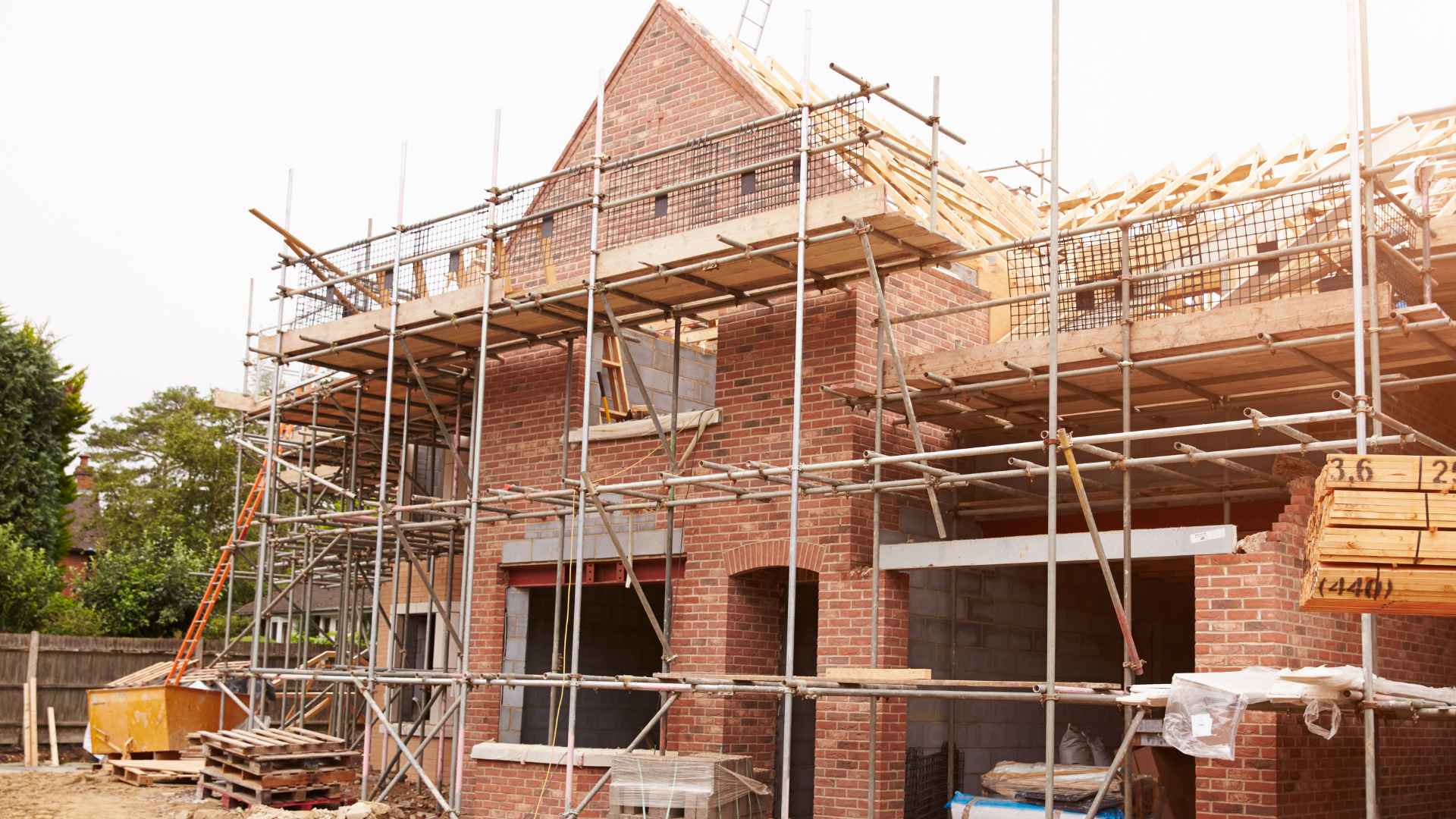 Single-family home under construction in the United States showing scaffolding and brick exterior, reflecting rising building costs.